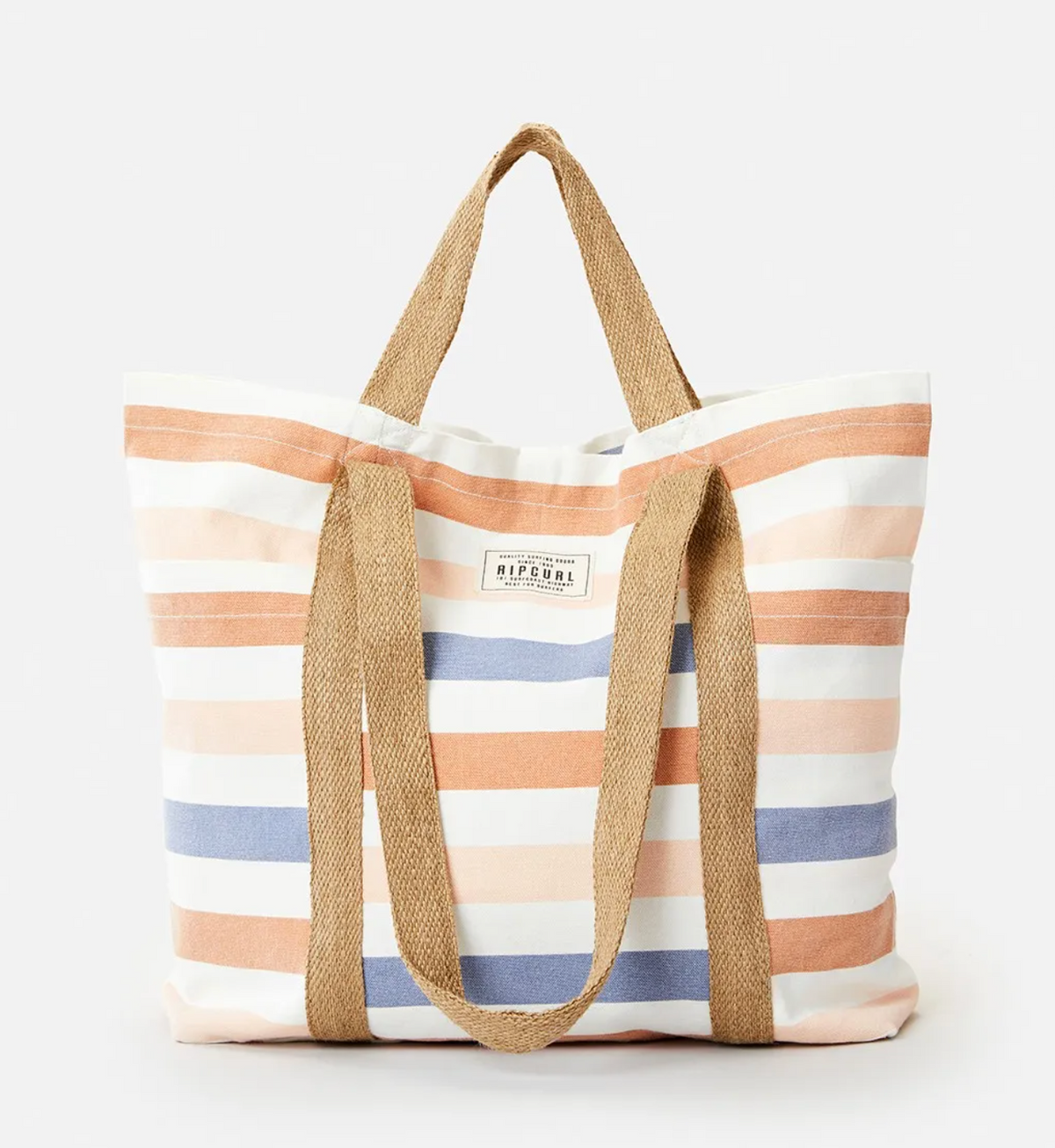The Rip Curl Organic 29L Beach Tote is a striped canvas bag made from organic cotton, featuring horizontal stripes in orange, blue, and cream. It has dual brown fabric handles and a small rectangular label on the front, standing out against its plain white background.