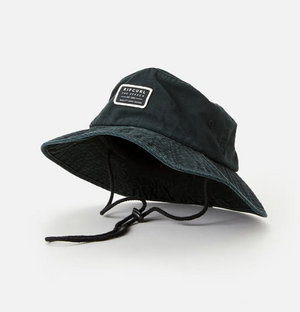 The Rip Curl Crusher Wide Brim Hat, a black cotton twill bucket hat, rests on a white background. It has an adjustable chin cord and features a rectangular patch with text on the front.