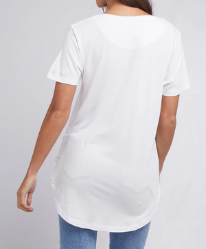 A person is seen from the rear in a Silent Theory Zuri Tee, crafted from cotton/bamboo jersey, paired with light blue jeans. The tee hangs loosely for an effortlessly casual vibe against a plain light gray background as they stand slightly angled to the right.