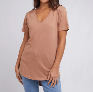 Wearing a Silent Theory Zuri Tee made of Cotton/Bamboo Jersey, a person in relaxed blue jeans stands against a plain background. Their left hand rests on their thigh, angled slightly right, embodying an effortlessly cool vibe with their head cropped out of the frame.