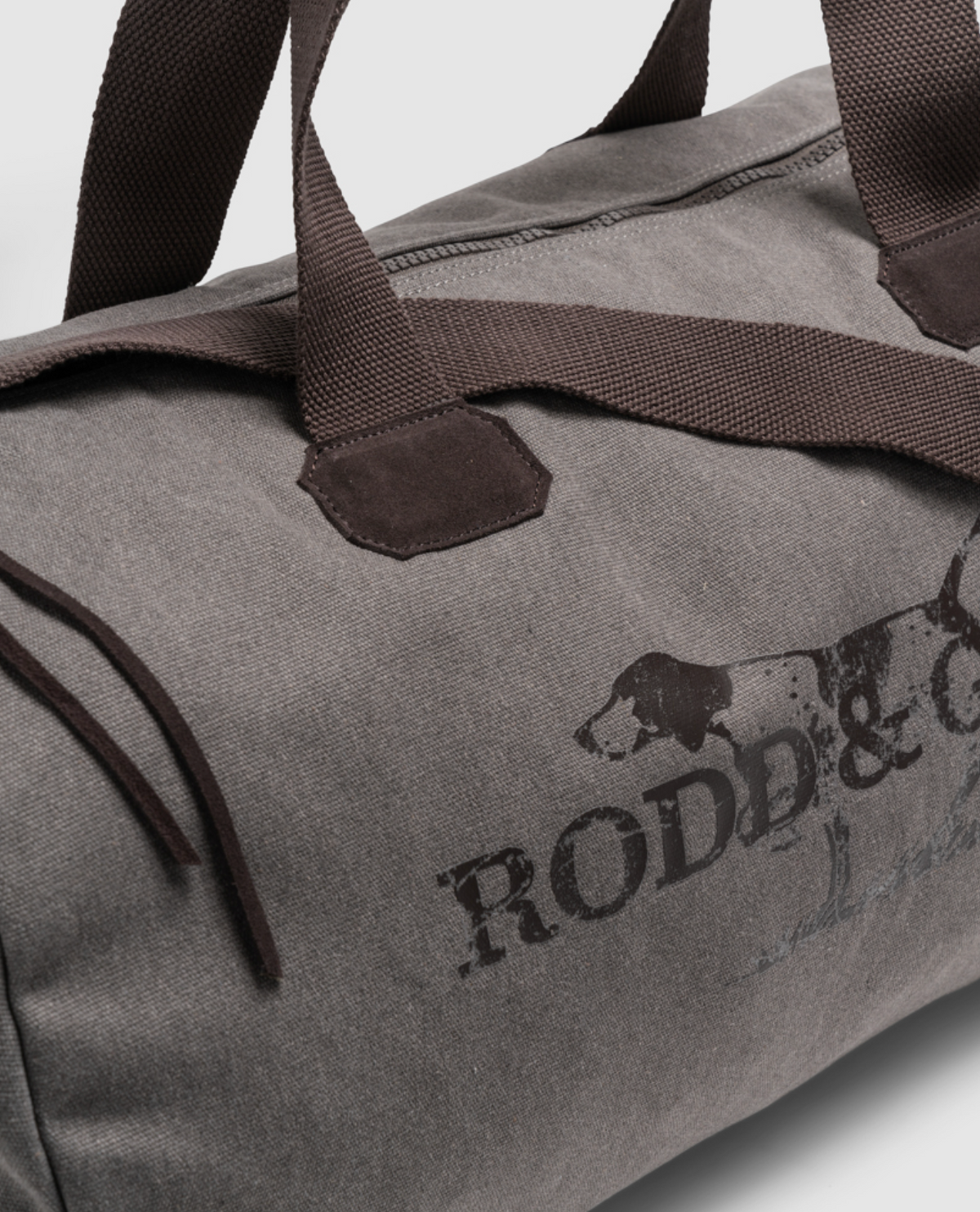 Close-up of the Rodd & Gunn Double Barrel Duffle Bag in gray cotton canvas with brown handles and a partial dog logo, featuring stylish functionality and durability for any adventure.