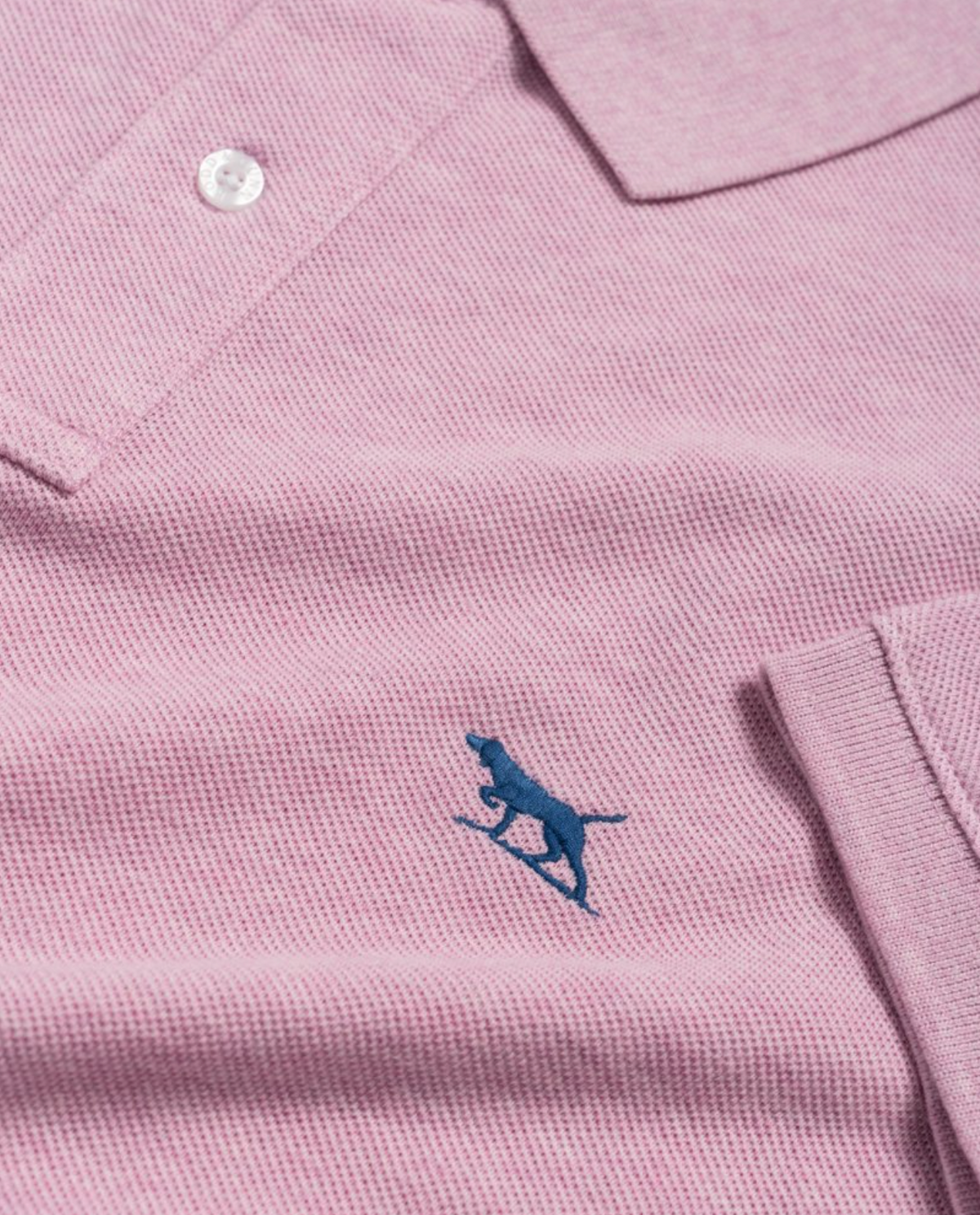 The Rodd & Gunn The Gunn Polo is a close-up of a light pink modern-fit polo shirt with a collar and one visible white button, crafted from premium Australian cotton. It features a small blue embroidered silhouette of a running cheetah on the fabric.