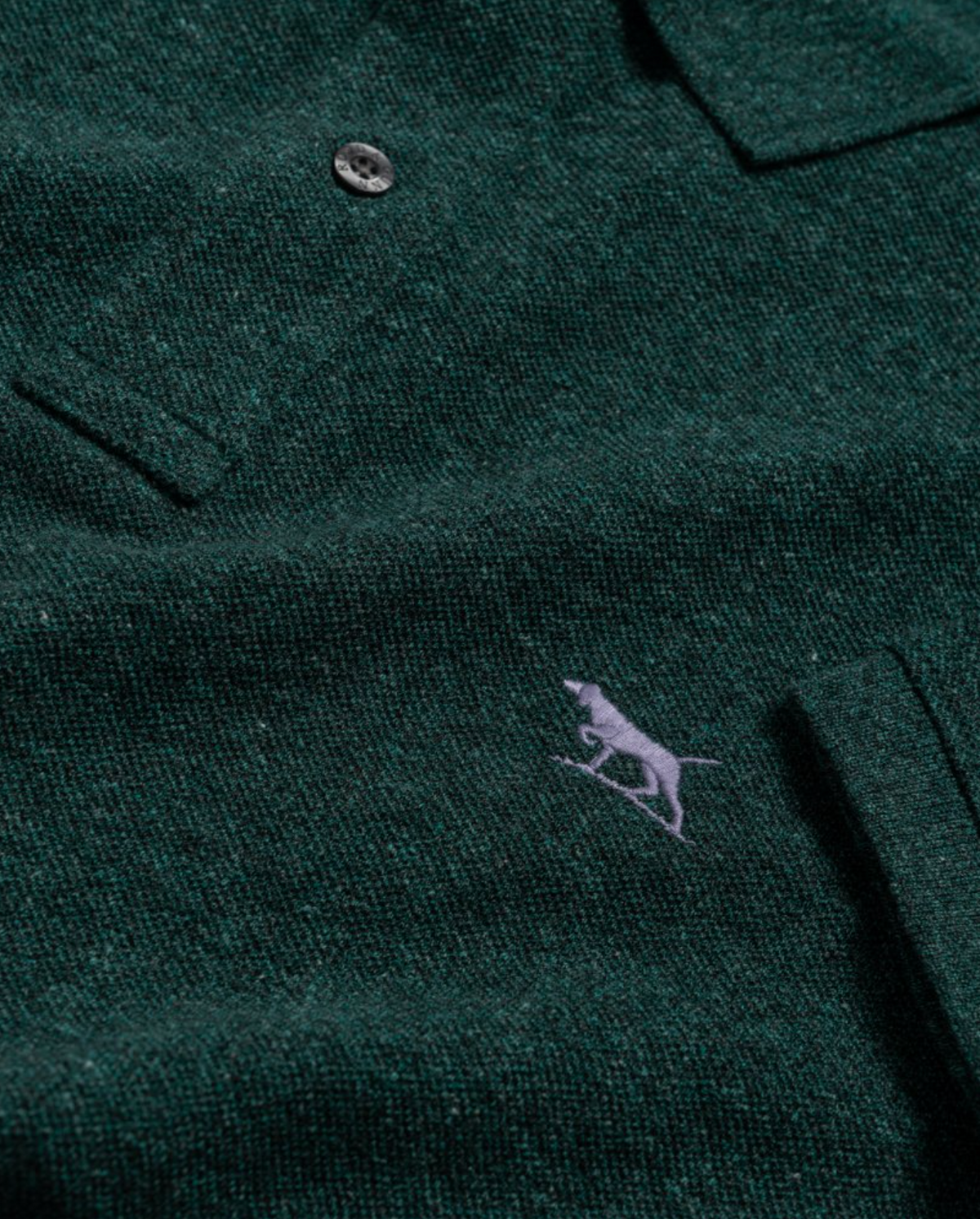 The Rodd & Gunn The Gunn Polo in dark green showcases a modern fit with a single button, textured premium Australian cotton, and a small light grey embroidered logo of a greyhound or similar dog.