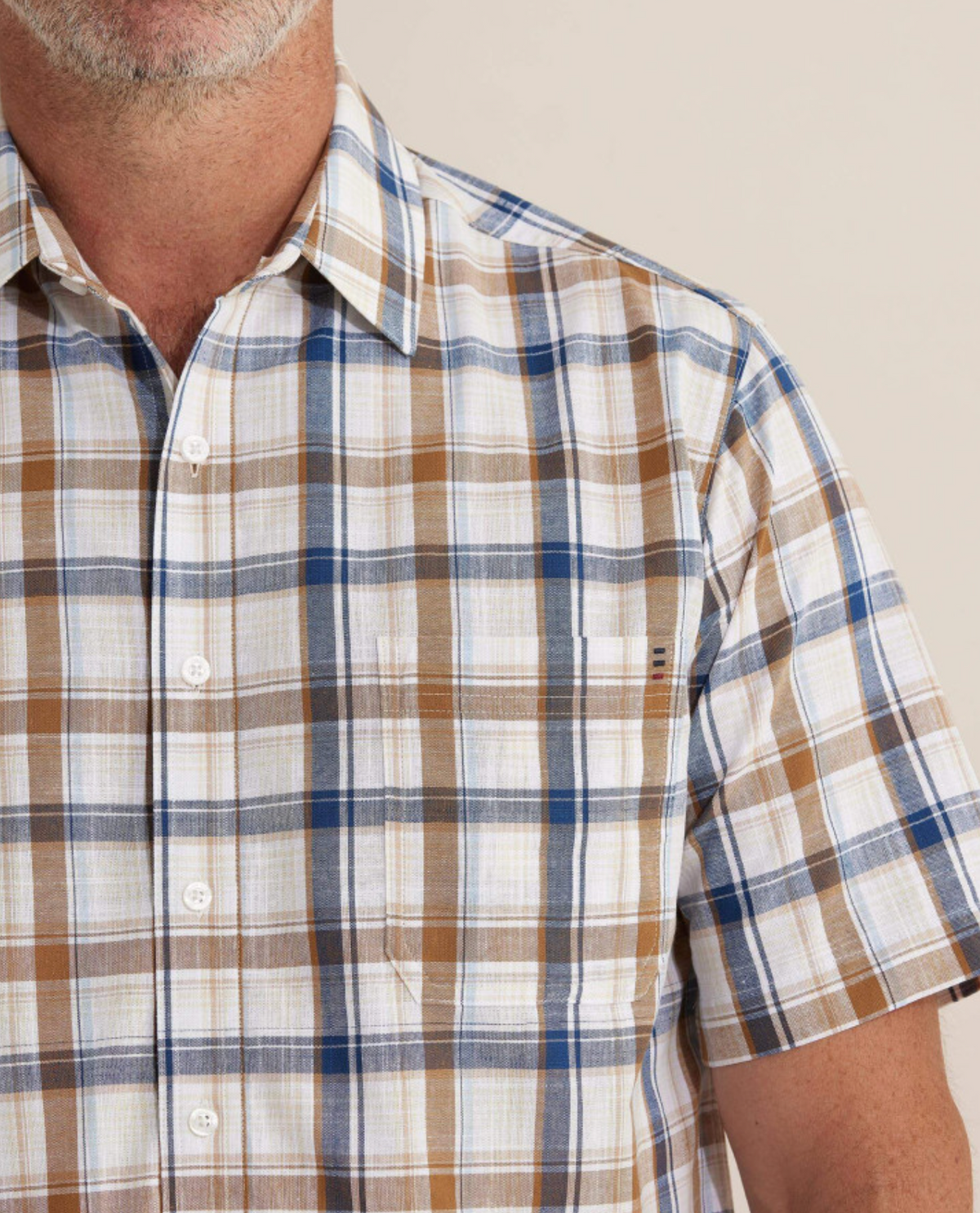 Someone wears the Breakaway Amber Flaxley Shirt, a comfortable, 100% cotton, short-sleeved button-up with a plaid pattern in brown, blue, and white. The focus is on the upper body against a neutral backdrop.