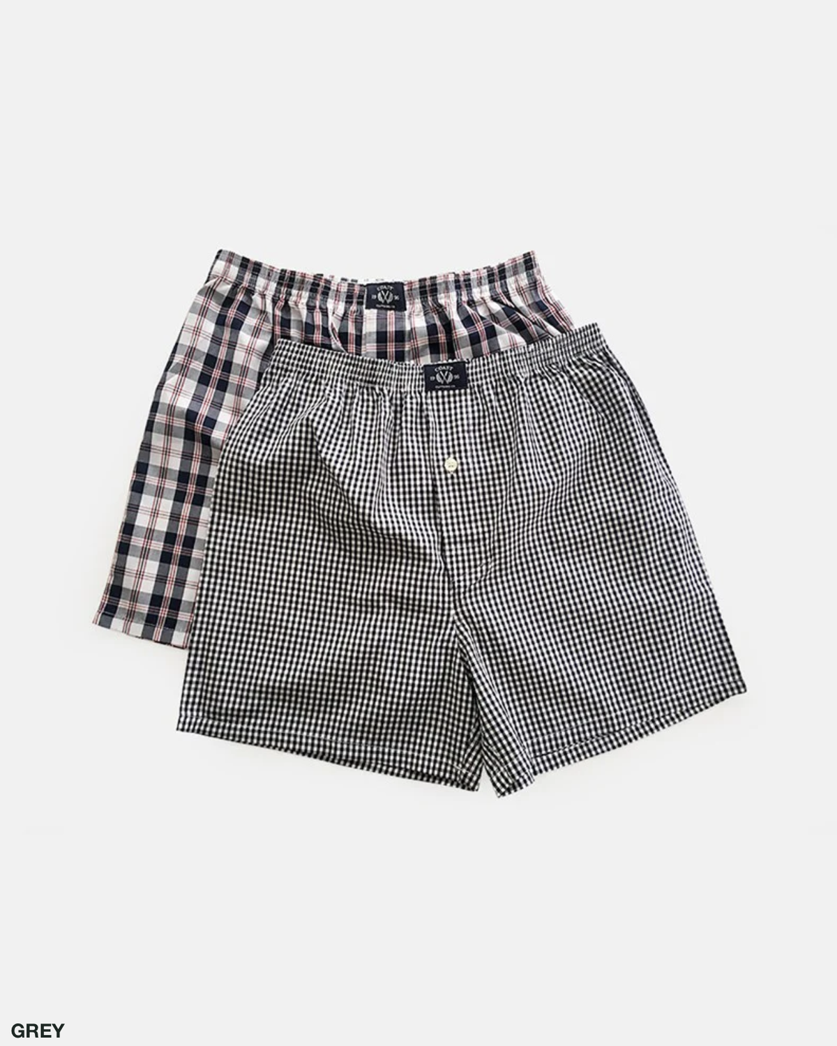 Two pairs of Coast Clothing Woven Check Boxers are laid flat on a white background. One pair features a grey and white small checkered pattern, while the other boasts a larger plaid design in grey, black, and white hues. Made from 100% cotton, both pairs ensure ultimate comfort.