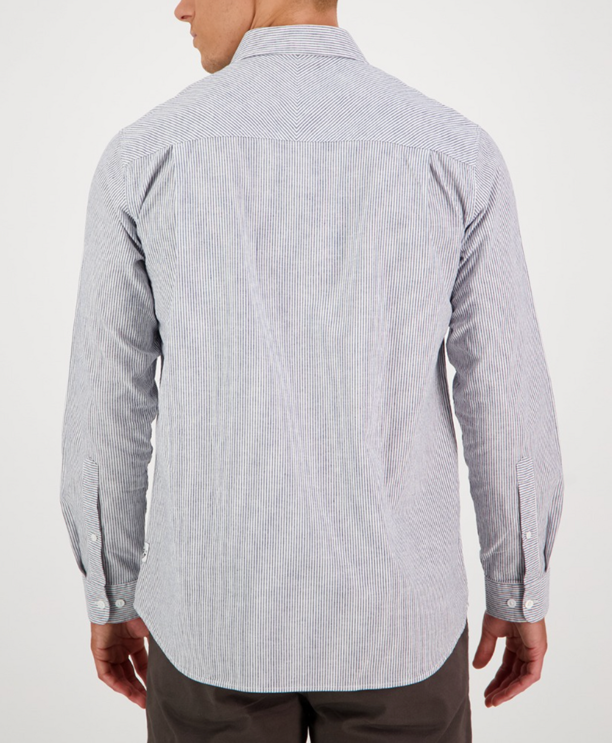 The Swanndri Carillo Beach L/S Shirt, featuring a comfortable blue and white stripe design and long sleeves, is paired with dark pants. The tailored fit enhances the relaxed style as the person stands against a plain white background.
