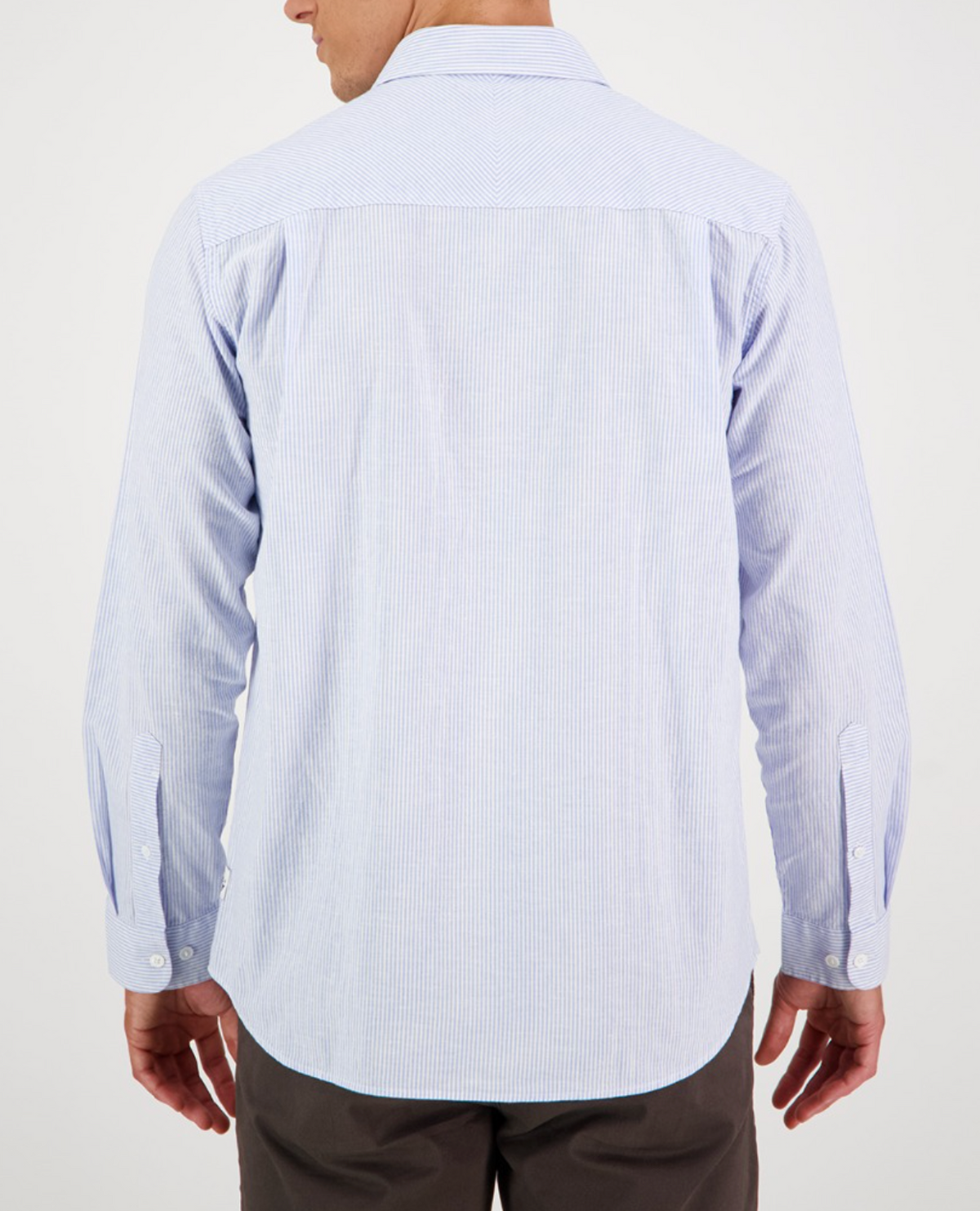 Seen from the back, a person wears a Swanndri Carillo Beach L/S Shirt in light blue with subtle stripes. The comfortable, casual-fit shirt has long sleeves and is tucked into dark pants.