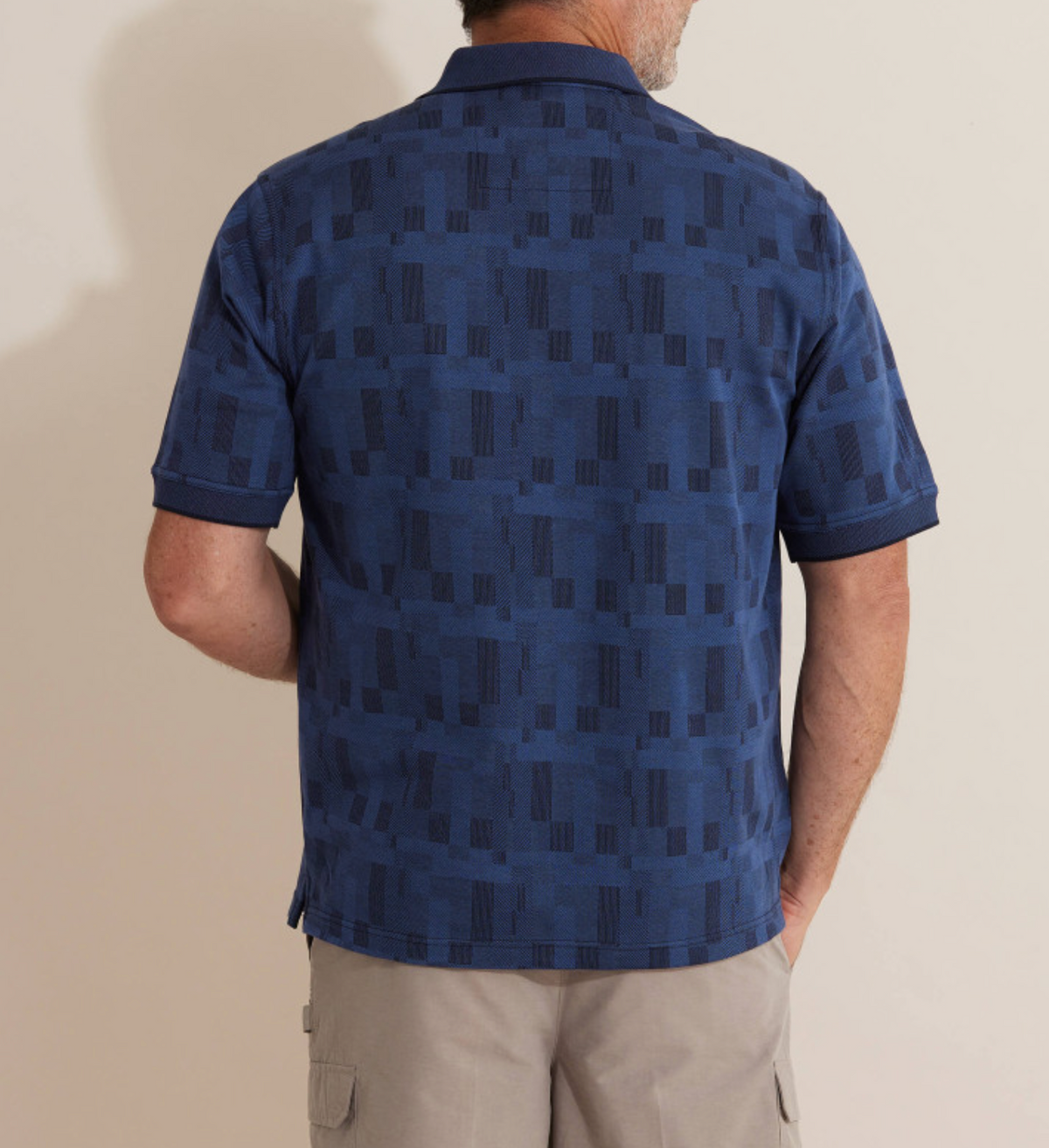 A man in a Breakaway Jacquard Micro Prima Polo and beige cargo shorts stands casually, back to the camera. His right hand is in his pocket against a plain background, exuding comfortable ease.