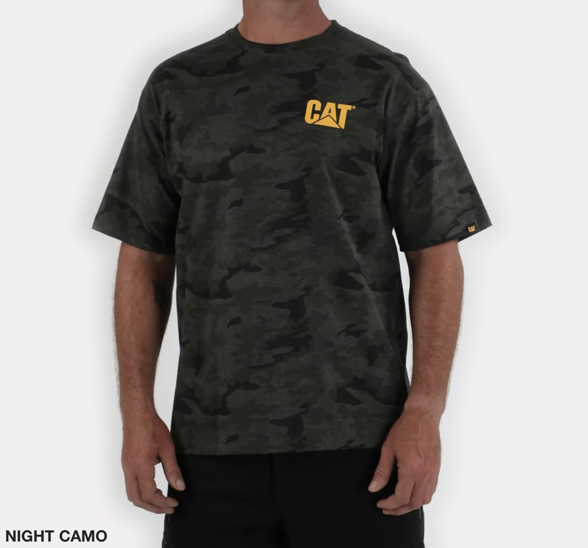 A person wearing the CAT Trademark Tee, a 100% cotton casual shirt in dark green and black camouflage with a yellow "CAT" logo on the upper left chest. The "NIGHT CAMO" text decorates the bottom left corner against a white background.
