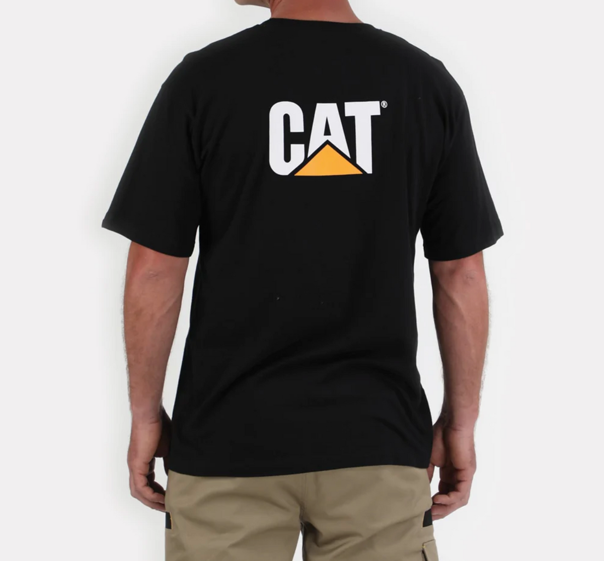 A person wearing the CAT Trademark Tee, featuring 100% cotton and a unique "CAT" logo with an orange triangle, is facing away. They are paired with khaki shorts against a plain white background.