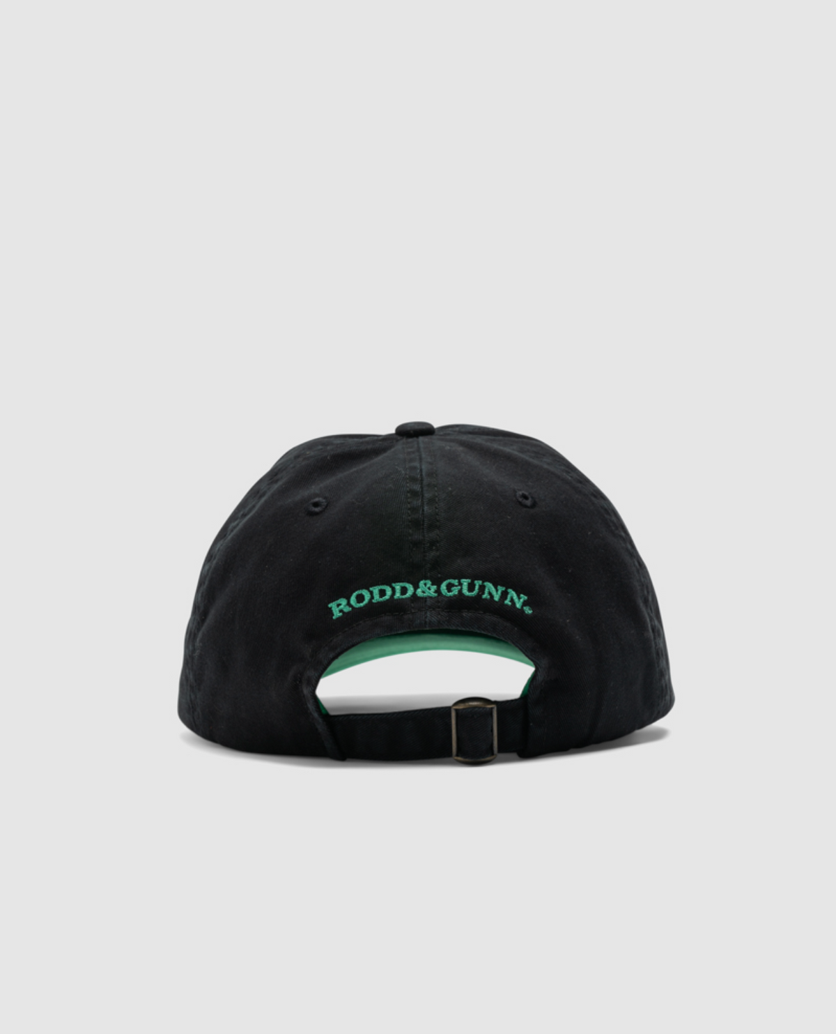 The Rodd & Gunn Gunn Cap, seen from the back, is made of durable cotton twill and sports "RODD & GUNN" embroidered in green above an adjustable strap with a metal buckle, all set against a light gray background.