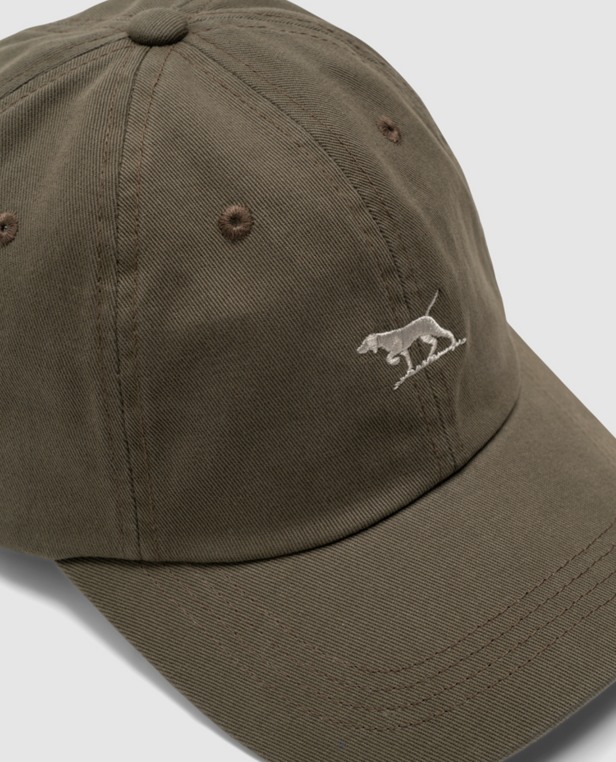 A Rodd & Gunn Gunn Cap in brown, made from heavy-duty cotton twill, showcases an embroidered white dog on the front and is set against a light gray background.