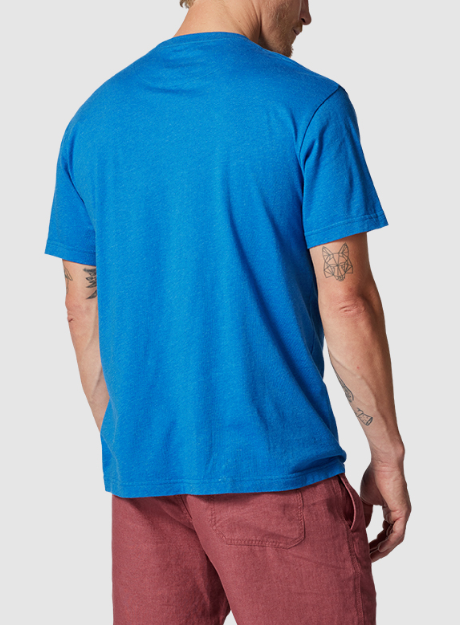 A person in a blue Rodd & Gunn The Gunn T-Shirt, made from premium Australian Cotton and designed in a sports fit, pairs it with red shorts while facing away from the camera. Their T-shirt beautifully complements their arm tattoos, including a butterfly on the left forearm.