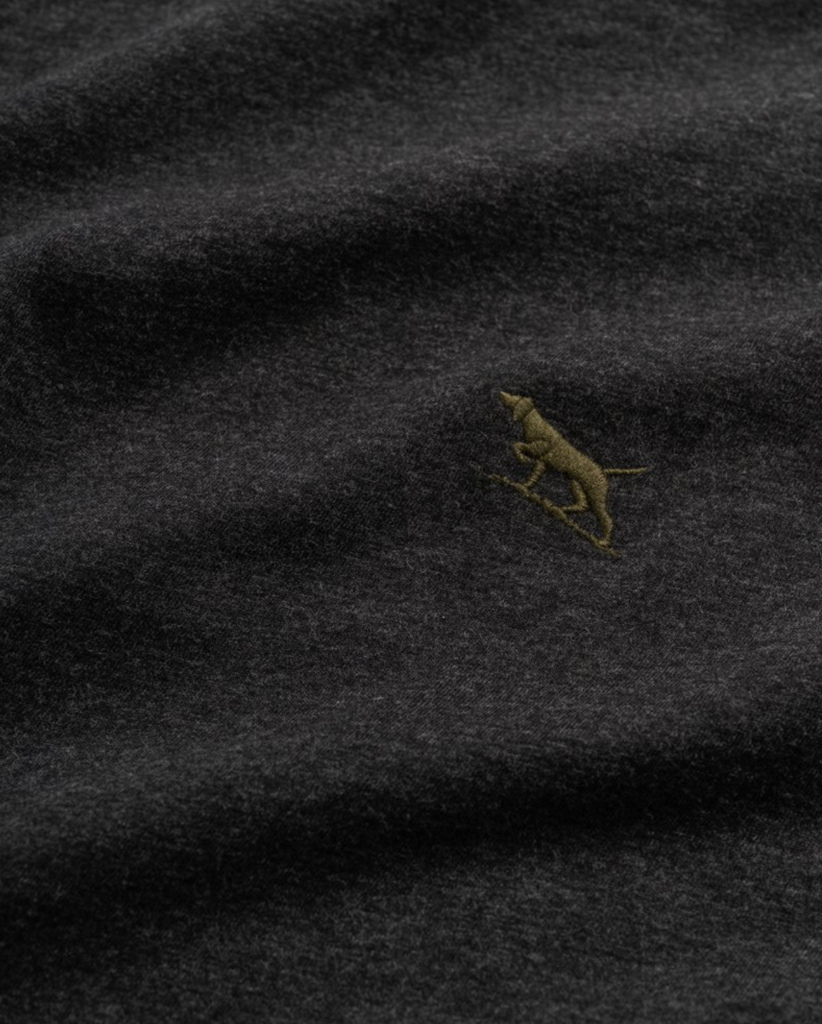 Close-up of Rodd & Gunn The Gunn T-Shirt, a dark gray fabric tee featuring a small embroidered yellowish-brown dog figure. Made from soft Australian cotton, it boasts a gentle and slightly textured feel.