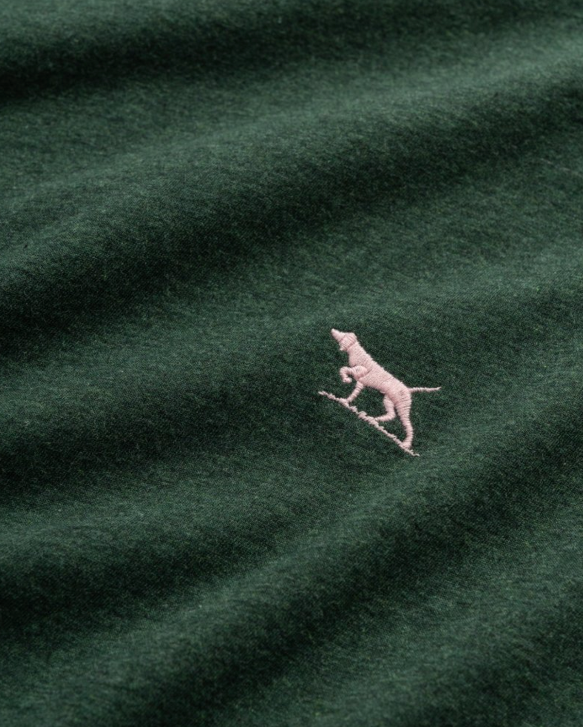 The Rodd & Gunn The Gunn T-Shirt, made from Australian Cotton, showcases a dark green color with a small pink dog embroidered over a diagonal line. Its sports fit offers both comfort and style for daily wear.