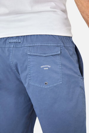 Someone is wearing Industrie The Bahama Angler Shorts in blue, which have an elastic waistband and a back pocket with "INDUSTRIE 1999" in white. Although they also wear a white t-shirt, the focus is on these stylish shorts adorned with the Industrie logo.