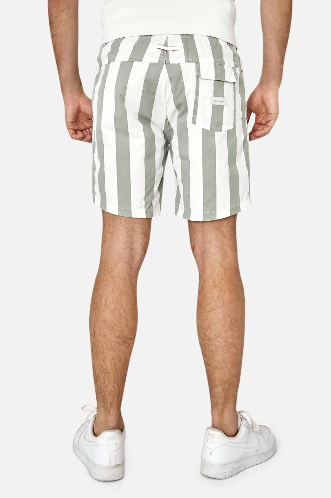 The photo showcases a rear view of someone wearing Industrie The Beverly Bahama Short, featuring gray and white vertical stripes, an elastic waist, and pockets, paired with white sneakers. The casual fabric and Industrie logo stand out against a plain white background.