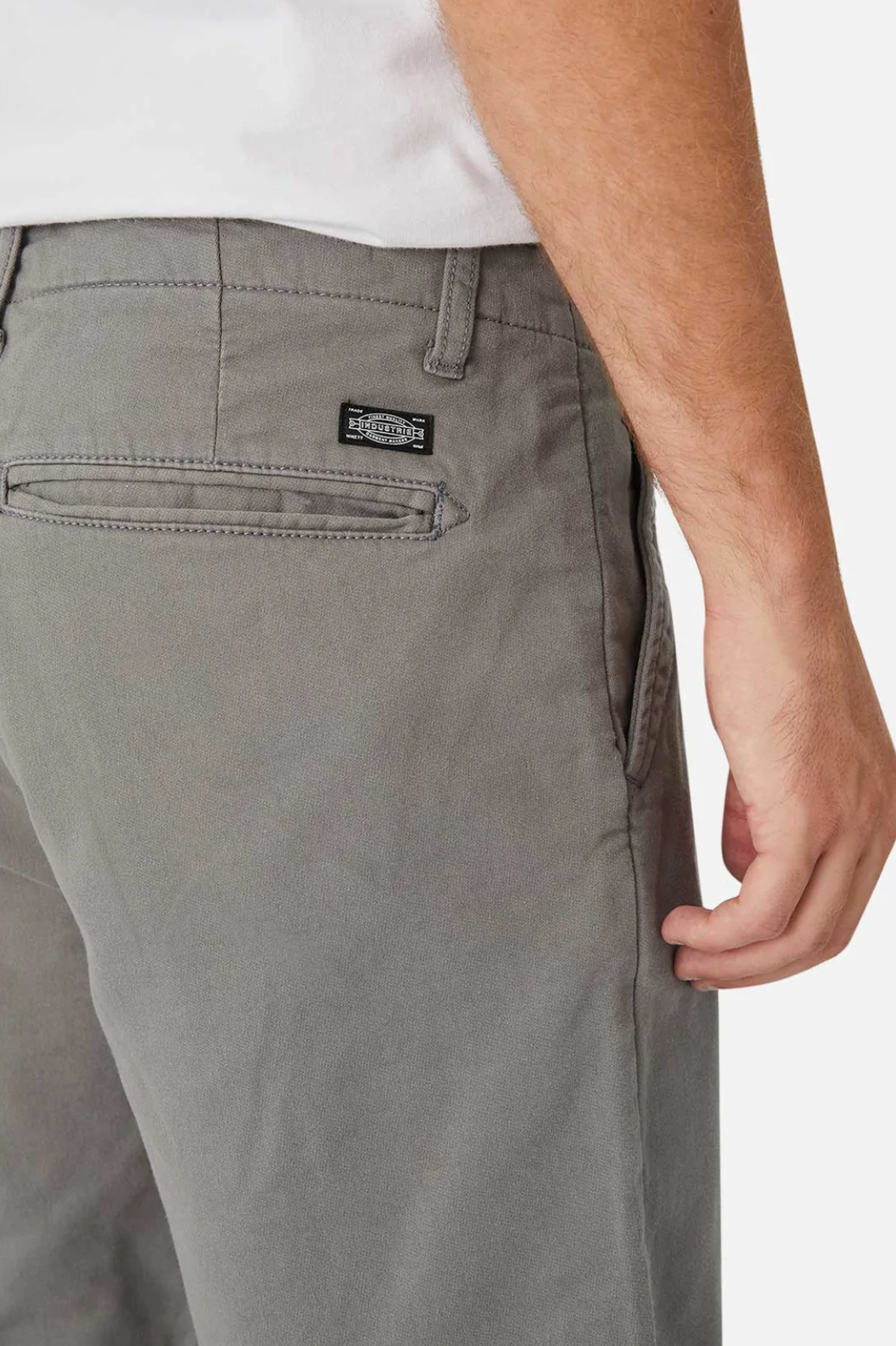 A person is wearing Industrie The Rinse Drifter Short in gray, with a hand in the pocket and a visible label near the back pocket. They sport a white shirt, and the image highlights the right side of their lower torso and hip area.