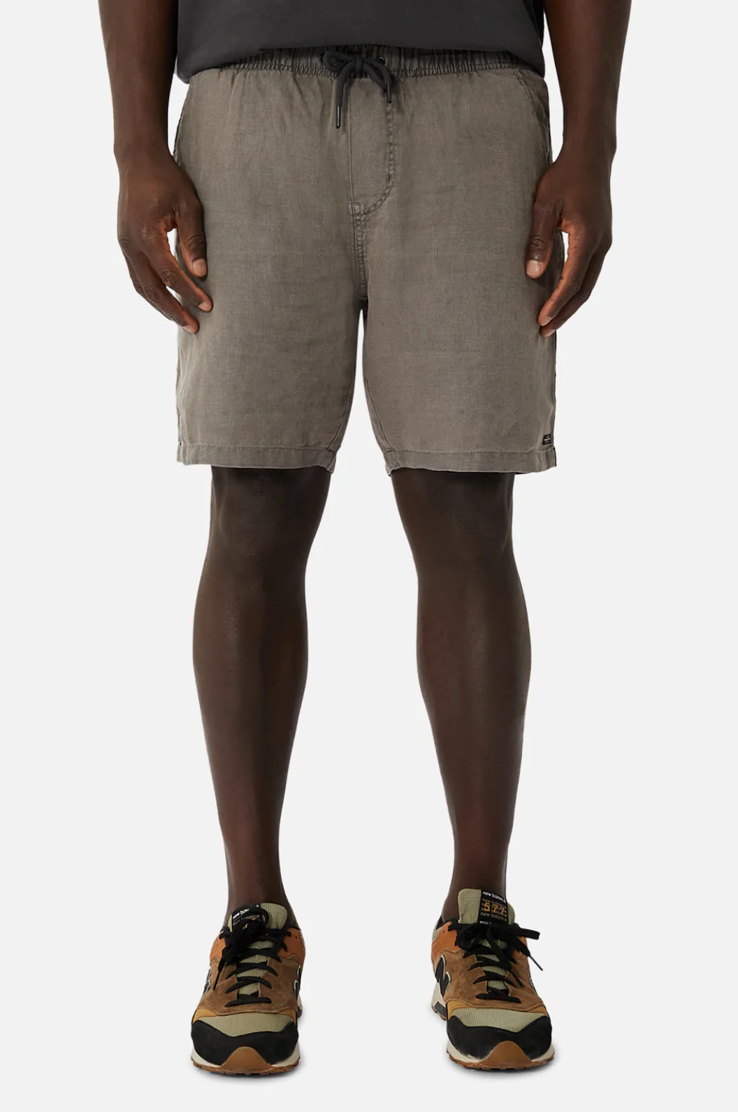 A man wears Industrie The Marina Linen Short in regular fit gray linen with an elastic drawstring waist, a black t-shirt, and tan and black sneakers, standing facing forward against a plain white background.