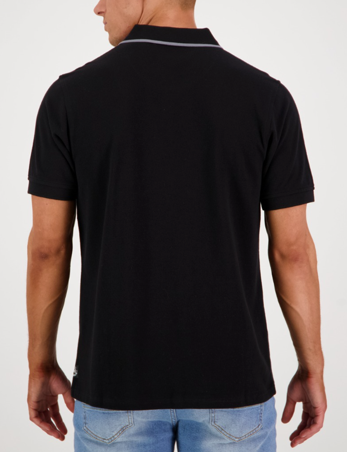 A person in a Swanndri Pinehurst Polo, made of black 100% cotton with a light gray striped collar, is shown from the back wearing blue jeans against a white background, subtly showcasing the embroidered logo.