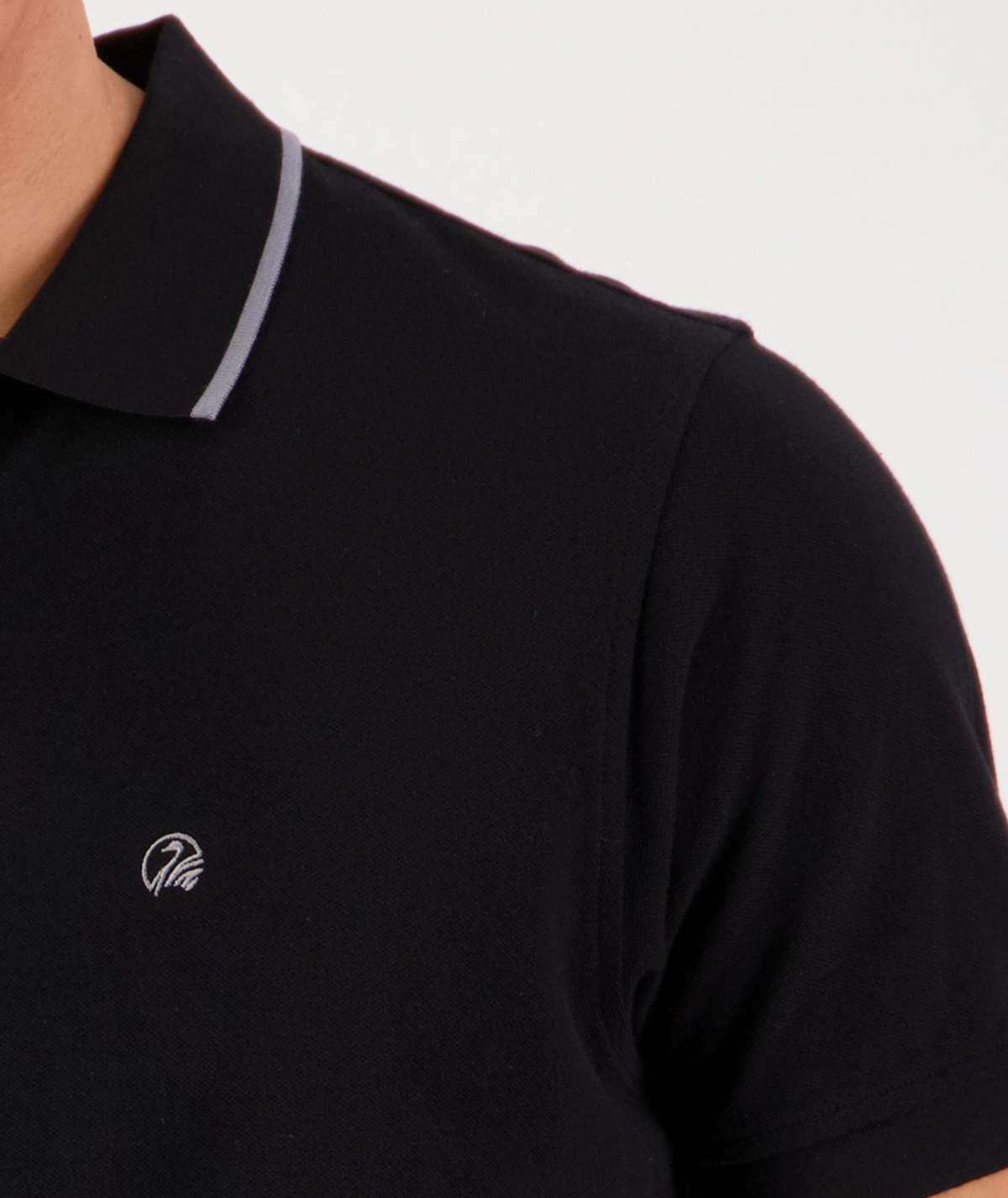 Close-up of a person wearing the Swanndri Pinehurst Polo, made from 100% cotton, with a thin light gray stripe on the collar and a small white embroidered logo on the chest. The background is plain white.