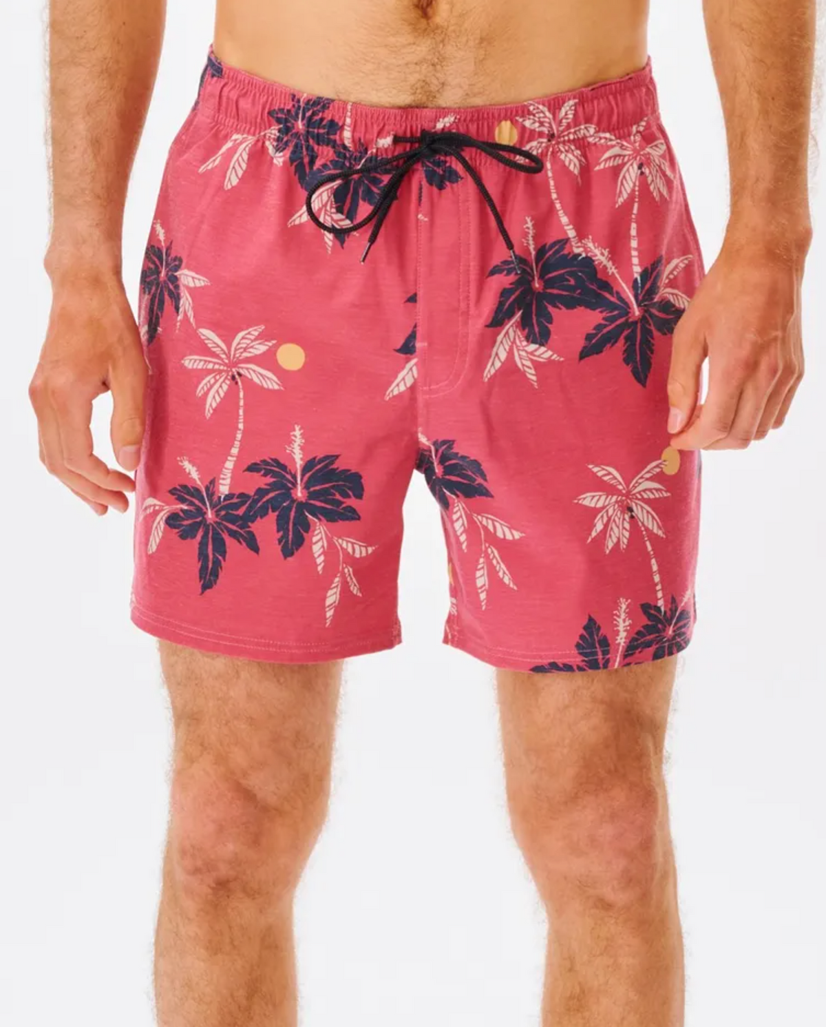 A person wears the Rip Curl Sumatra Volley Shorts, showcasing a pink pattern with blue palm trees and yellow circles. Made from quick-dry fabric, these shorts include an elastic waistband with a black drawstring. They stand against a plain white background.