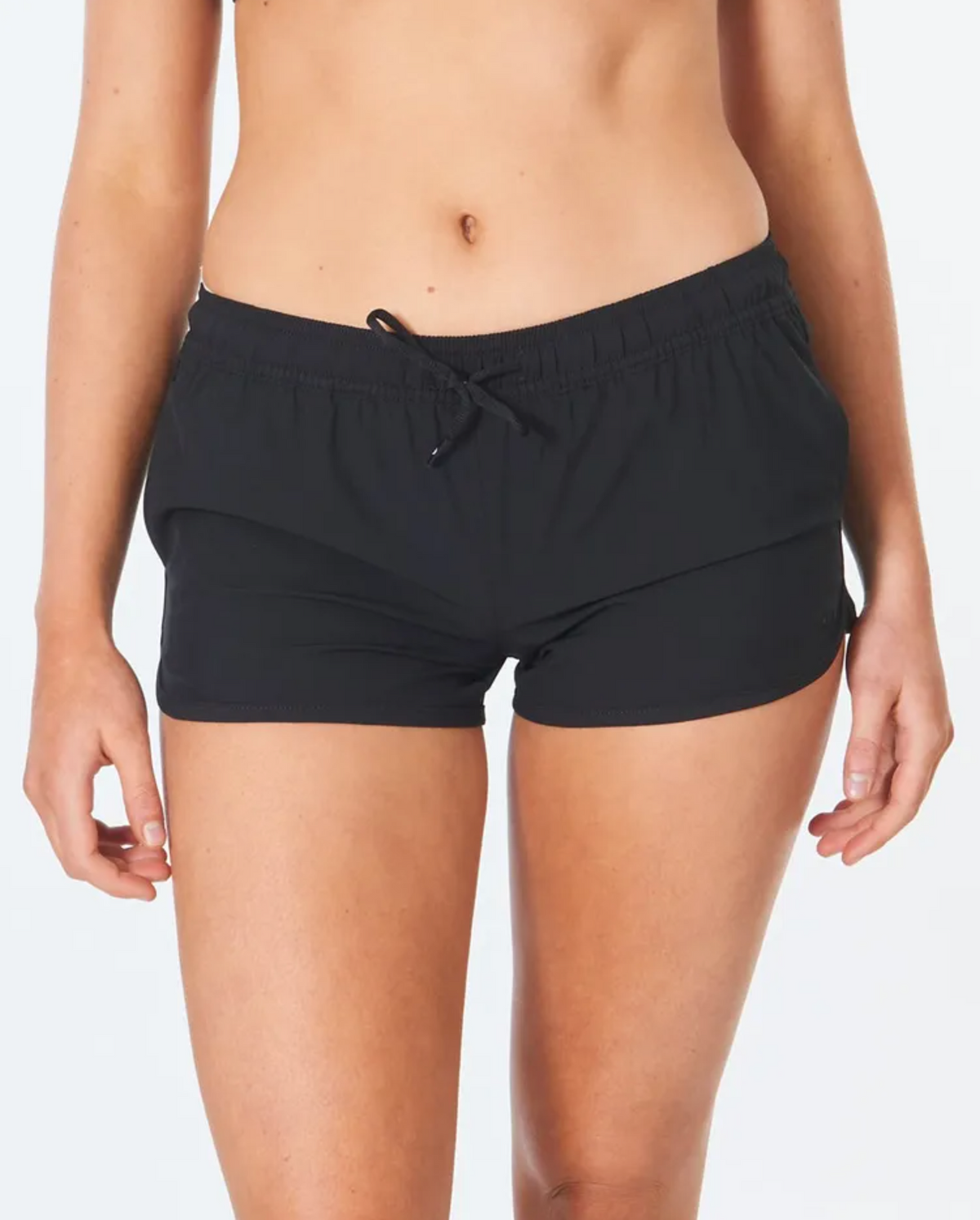 A person wears Rip Curl Classic Surf 3 Boardshort in black, crafted from recycled plastic bottles, against a white background. The focus is on the shorts with an elastic waistband and drawstring, made from 4-way stretch fabric. Visible is their lower torso to mid-thigh.