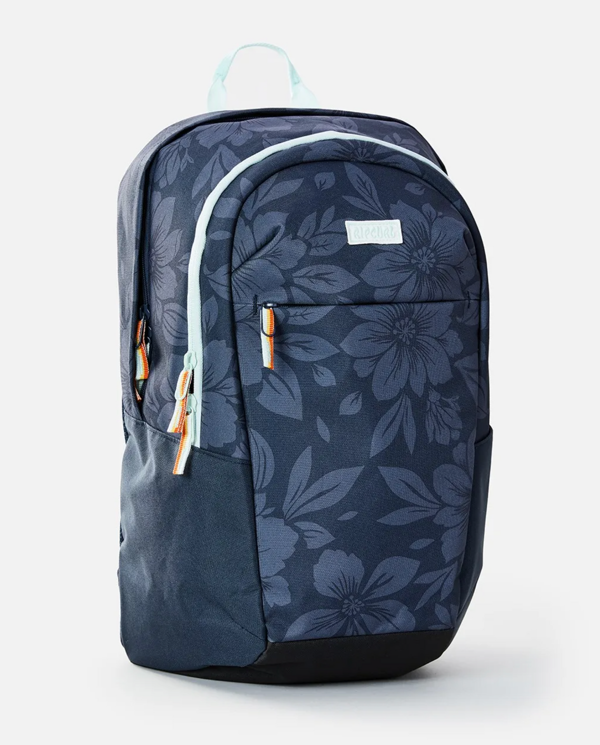 The Rip Curl Overtime 30L Backpack is made from recycled polyester, featuring a dark blue design with a large floral pattern, two main compartments suitable for a 15" laptop, light blue zippers with brown pulls, and a matching top handle on a plain white background.