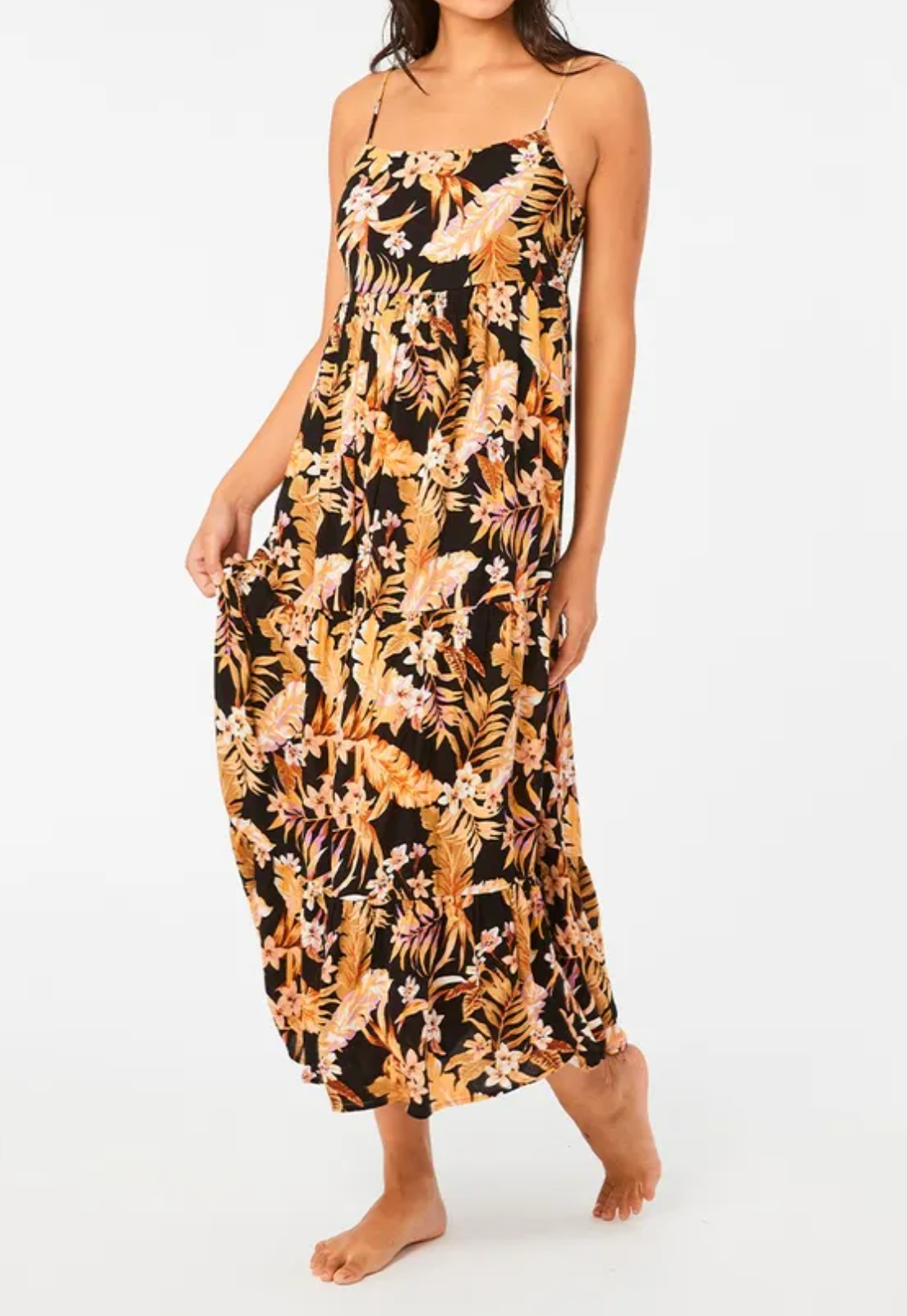 Barefoot on a neutral background, a person wears the Rip Curl Sunday Swella Midi Dress, a sleeveless black maxi crafted from EcoVero fabric with orange and pink floral patterns.