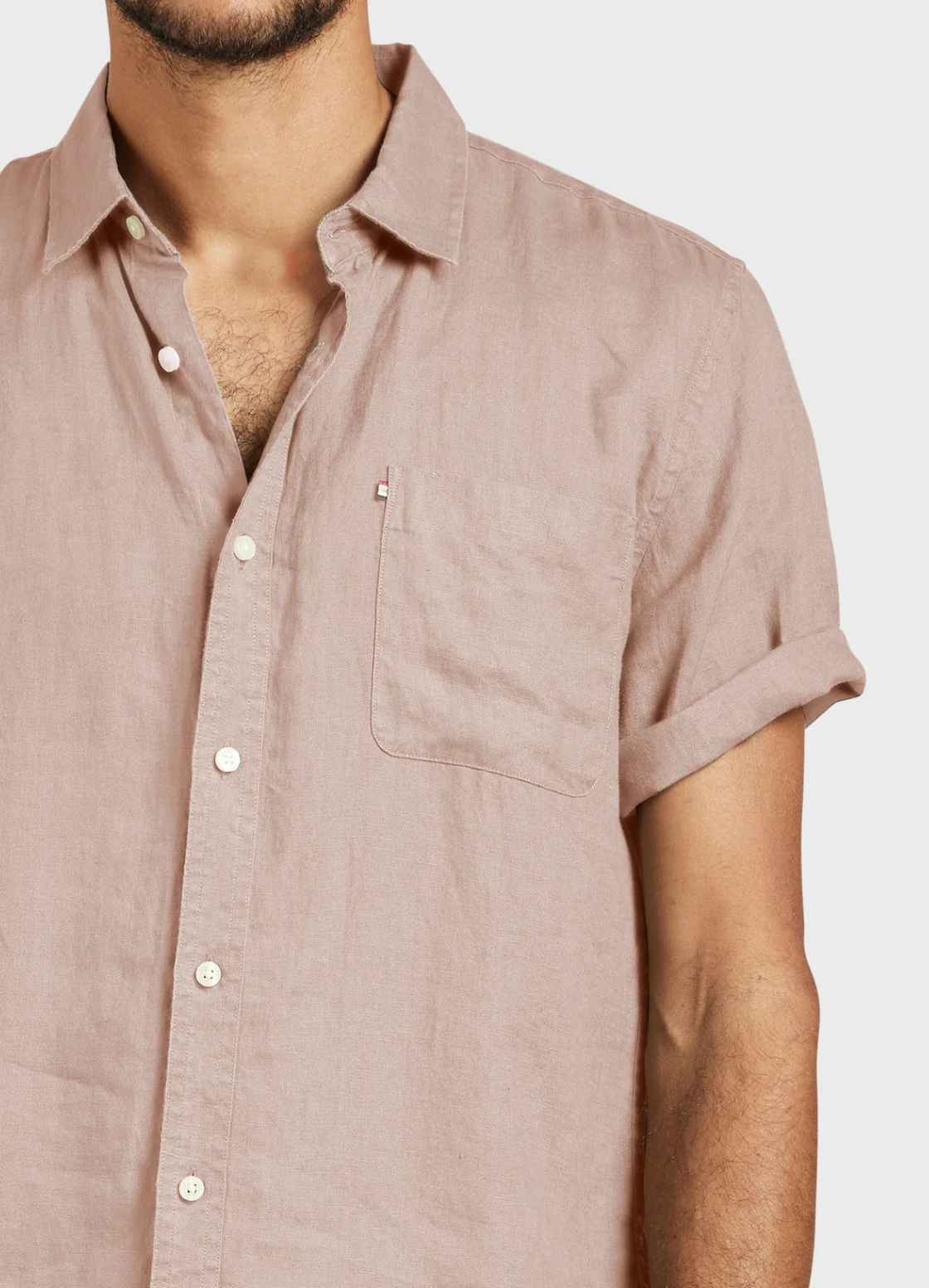 A man wears the Academy Brand Hampton Linen Short Sleeve Shirt in light pink, featuring a point collar and chest pocket. Only his torso and part of his face are visible against a plain background.