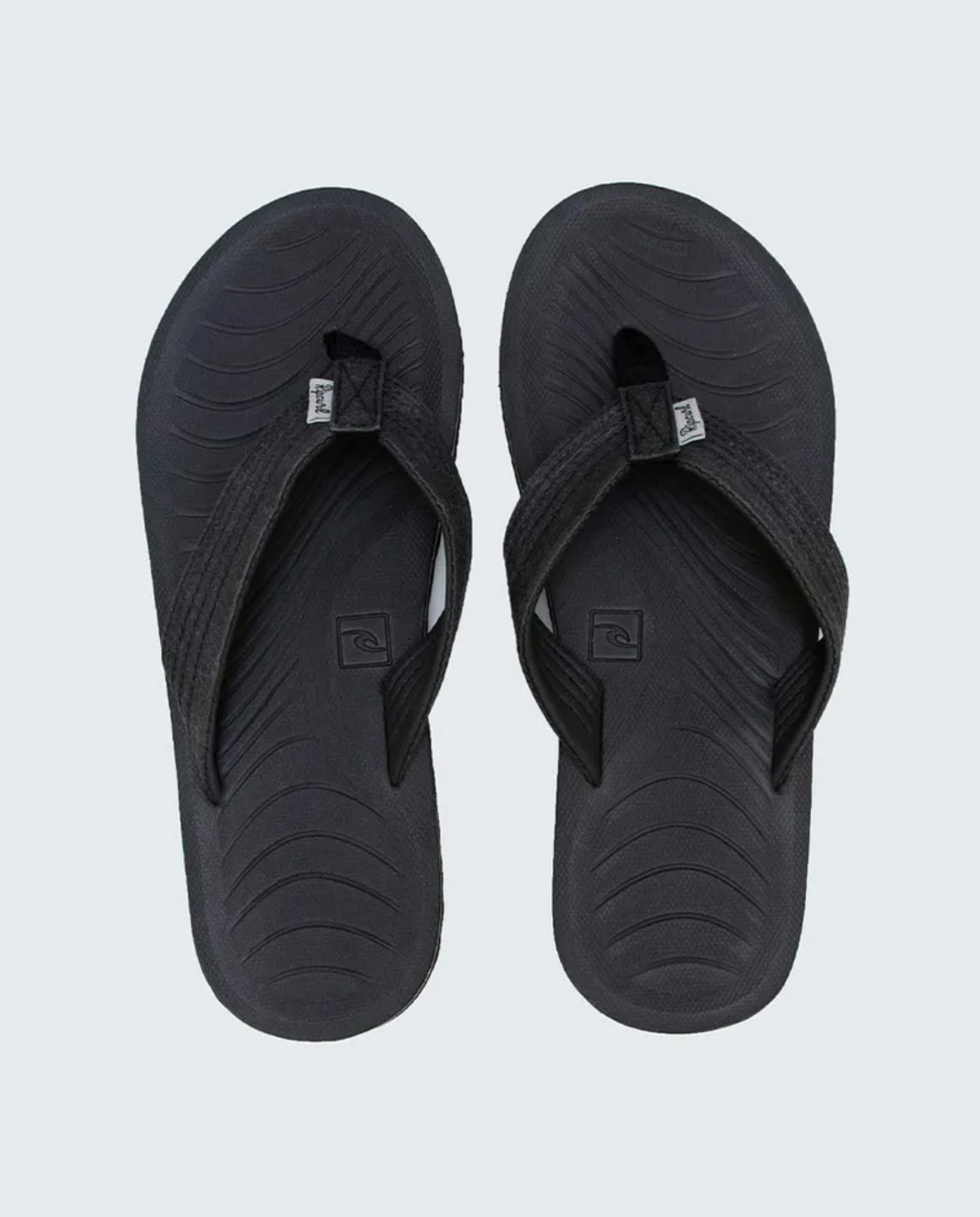 The Rip Curl D-Bah Sandle is a pair of black flip-flops with textured soles and straps made from recycled EVA. Each sandal has a small logo tag on the straps and an engraved logo on the footbed, set against a plain gray background.