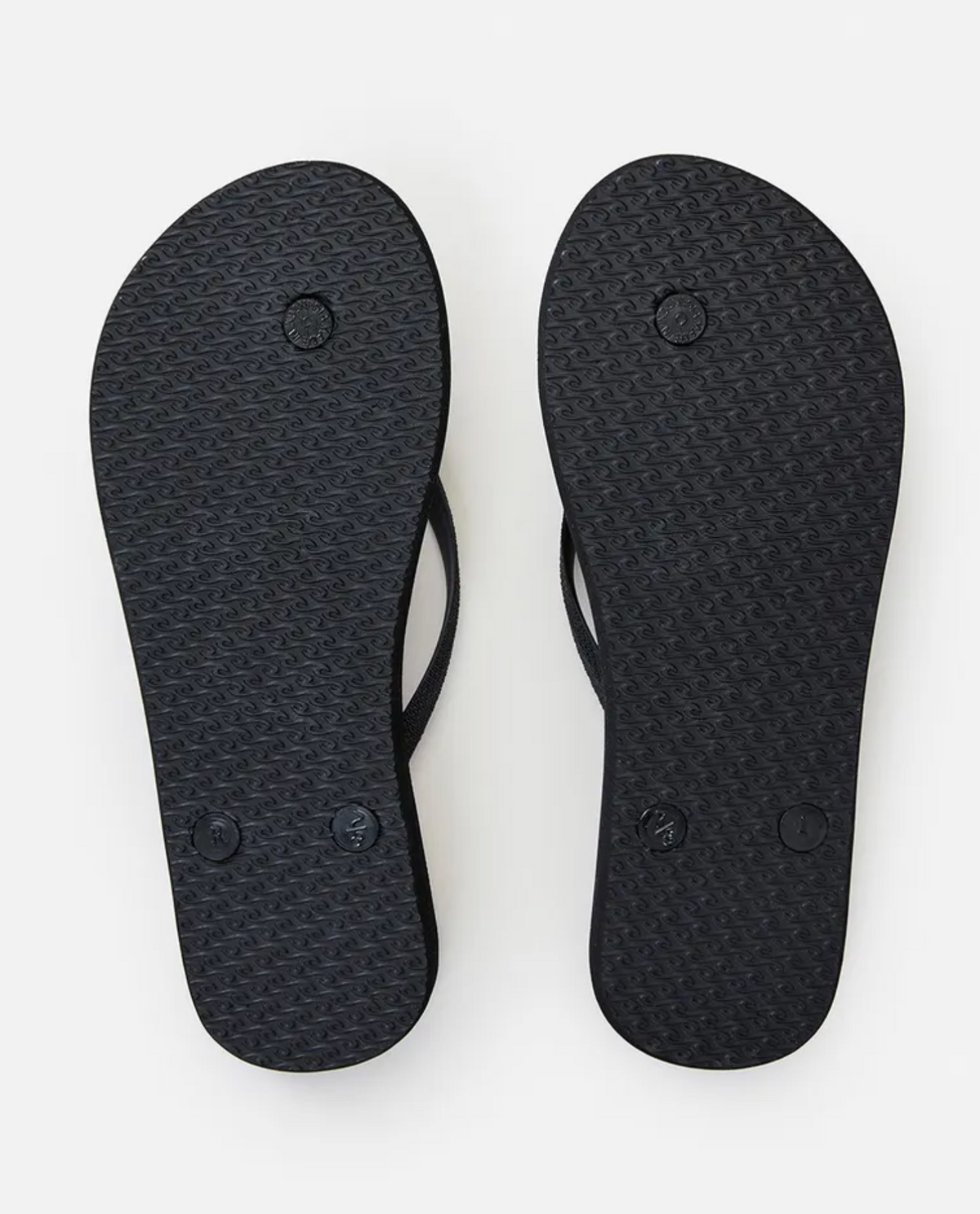 The Rip Curl Sunday Swell Thongs in black are shown from the bottom, highlighting their textured EVA rubber footbeds with circular patterns and small raised markings.