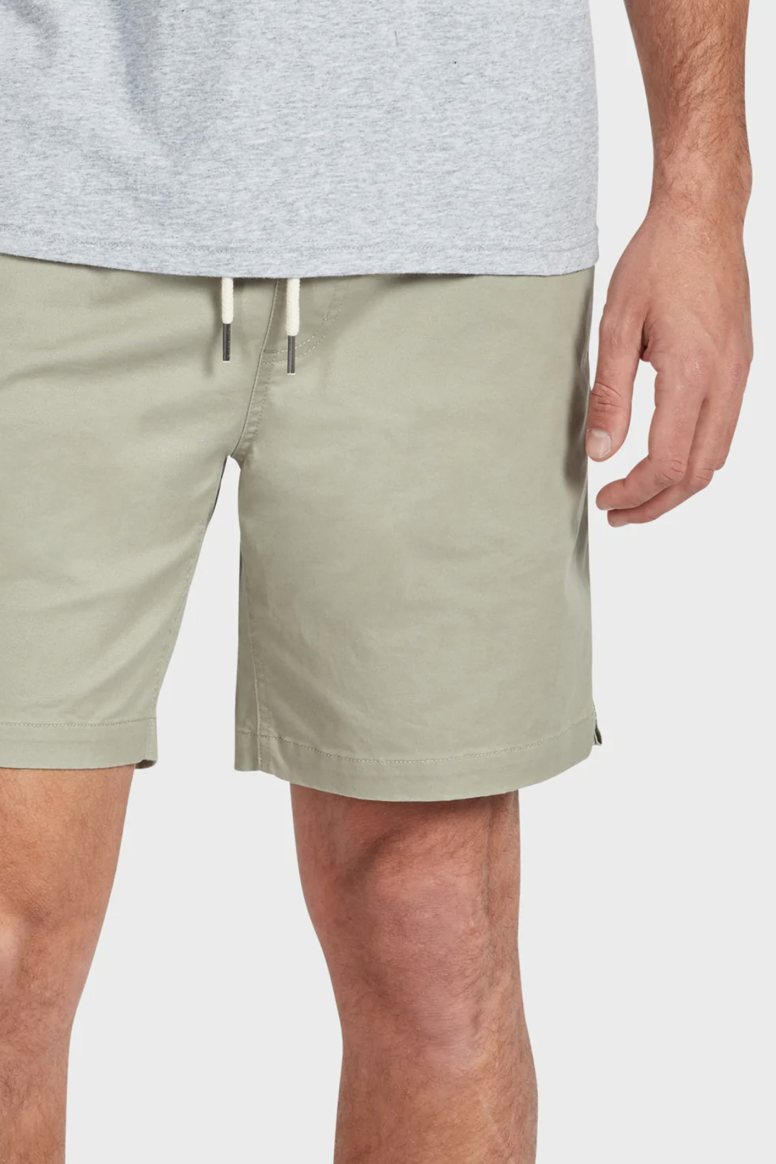 A person in a light gray cotton t-shirt and Academy Brand Volley Short in olive green stands with a relaxed hand by their side. The shorts have an elastic drawstring waist, and the image highlights the area from the waist to mid-thigh.