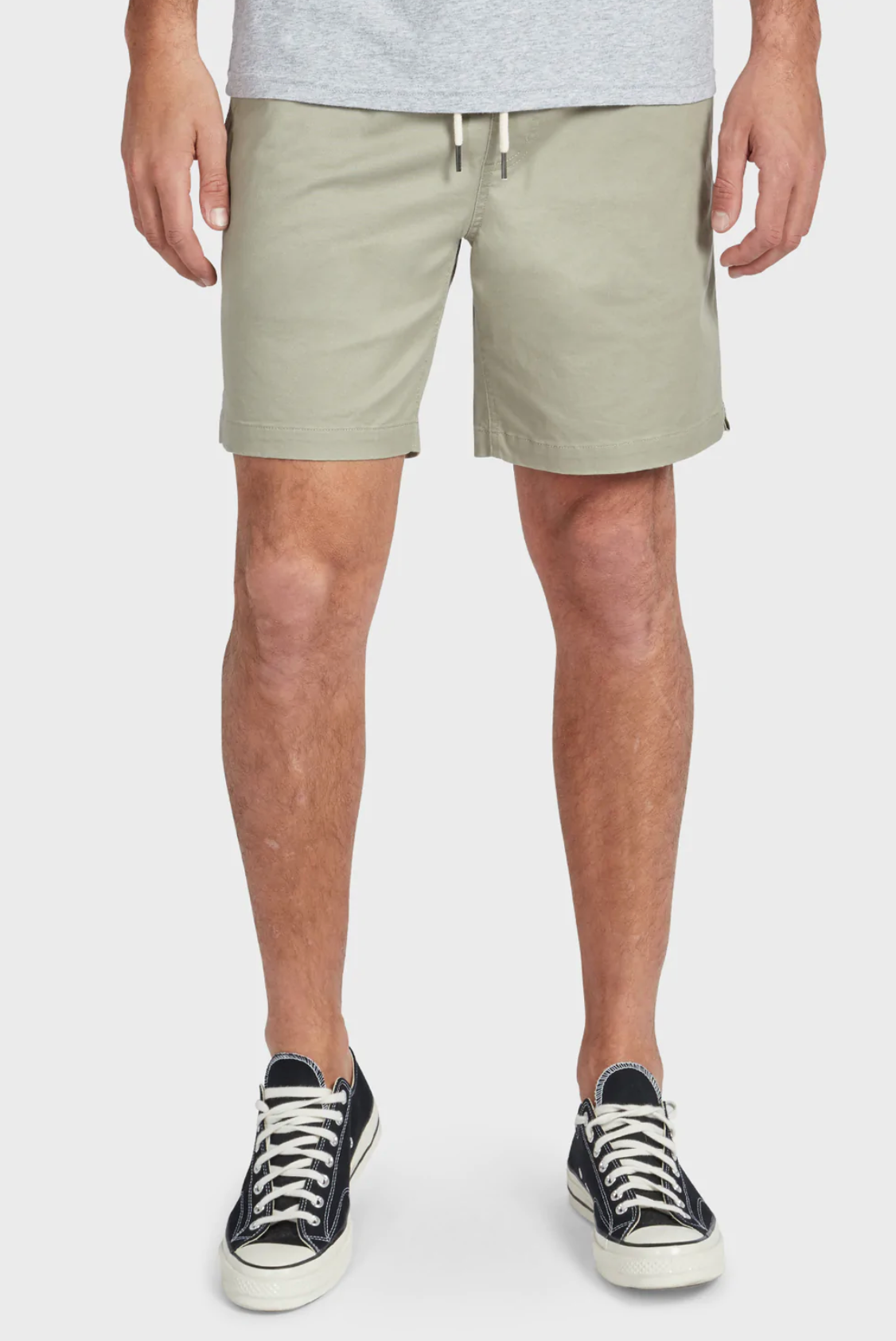 A person wears Academy Brand Volley Short in light gray with an elastic drawstring waist, a gray top, and black sneakers with white laces. The photo shows the lower half of their body against a plain white background.