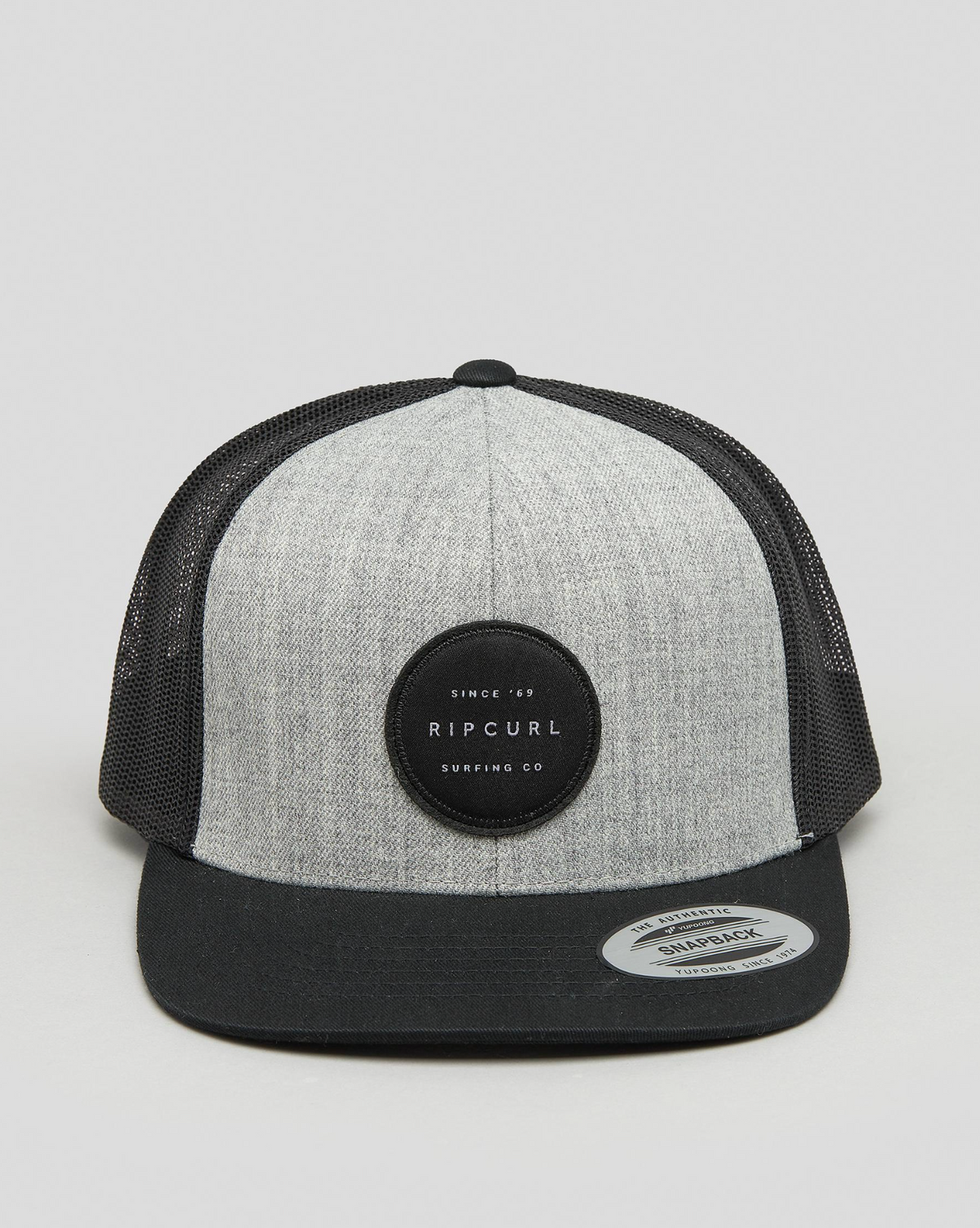 The Rip Curl Routine Trucker is a gray and black cap featuring a circular logo reading "Ripcurl Surfing Co." It includes a mesh back, flat black brim, and adjustable strap for optimal fit.