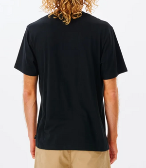 A person with long, curly blonde hair is seen from behind, wearing a black Rip Curl Corp Icon Tee made from 100% cotton and tan shorts, against a white background.