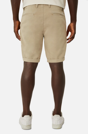 Viewed from behind against a plain white background, someone is wearing the Industrie The Rinse Drifter Short, which is beige and features comfortable cuffed hems and back pockets, paired with relaxed-fit white sneakers.