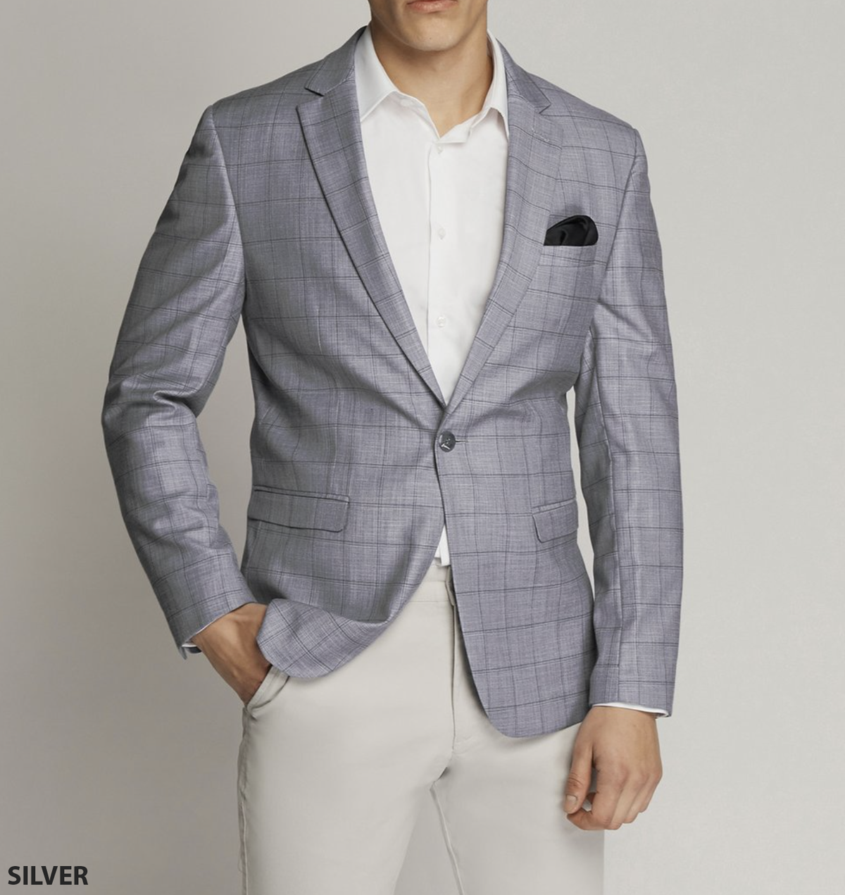 A man in a Scuzzatti Check Slim Fit Sports Jacket, light gray plaid design with black pocket square, paired with a white shirt and beige pants. One hand in his pocket, the other at his side. Check our size guide for a precise fit against the plain, light-colored backdrop.