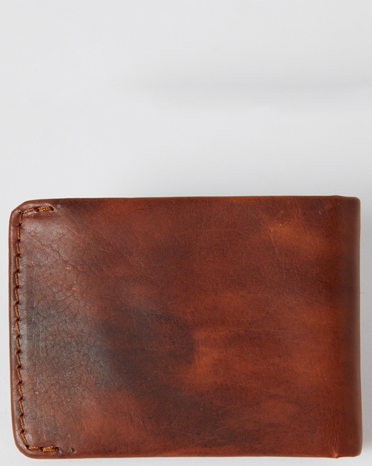 The Rip Curl Corpo RFID Slim Wallet is crafted from brown nubuck leather with visible edge stitching, set against a plain gray background. Its surface features a slightly weathered texture, enhancing its character.