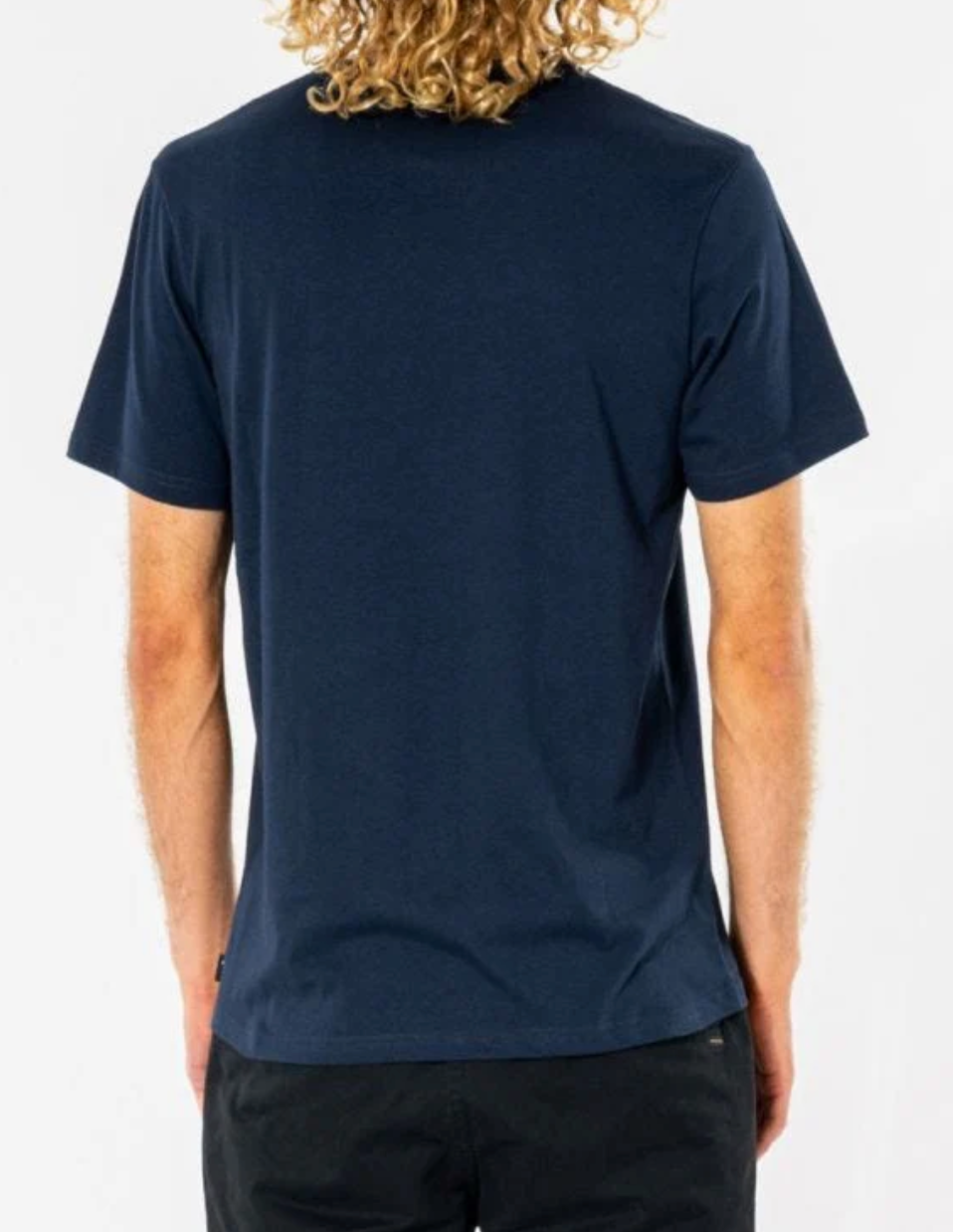 A person with curly blonde hair is wearing a navy blue Rip Curl Big Mumma Icon Tee and black pants, shown from the back against a plain white background.