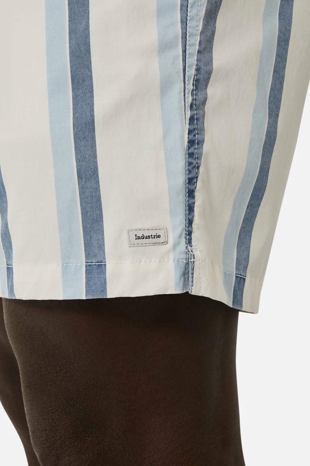 Close-up of a person wearing Industrie The Rubio Bahama Short in light blue and white vertical stripes, with an elastic waist and a small "Industrie" tag, set against a neutral background.