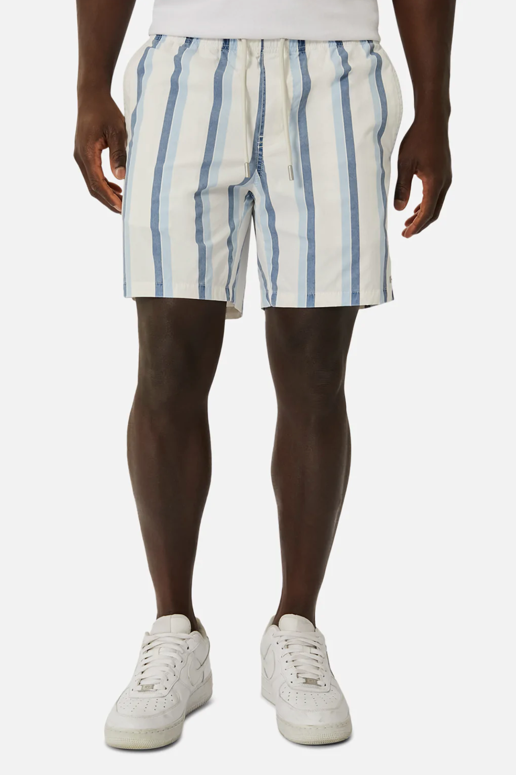 A person in a white shirt and Industrie The Rubio Bahama Shorts with blue and white vertical stripes and an elastic waist, paired with white sneakers. The background is plain white.