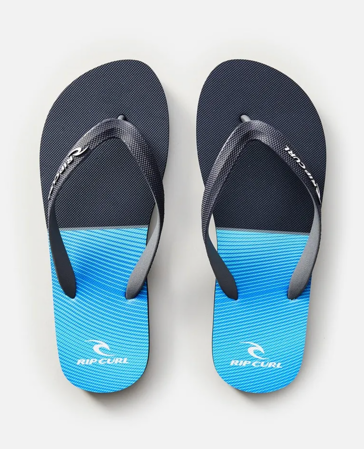 Rip Curl Iconic Thongs with dark blue rubber straps and gradient soles, transitioning from black at the heel to light blue at the toes, prominently displaying the Rip Curl logo on both straps and soles.