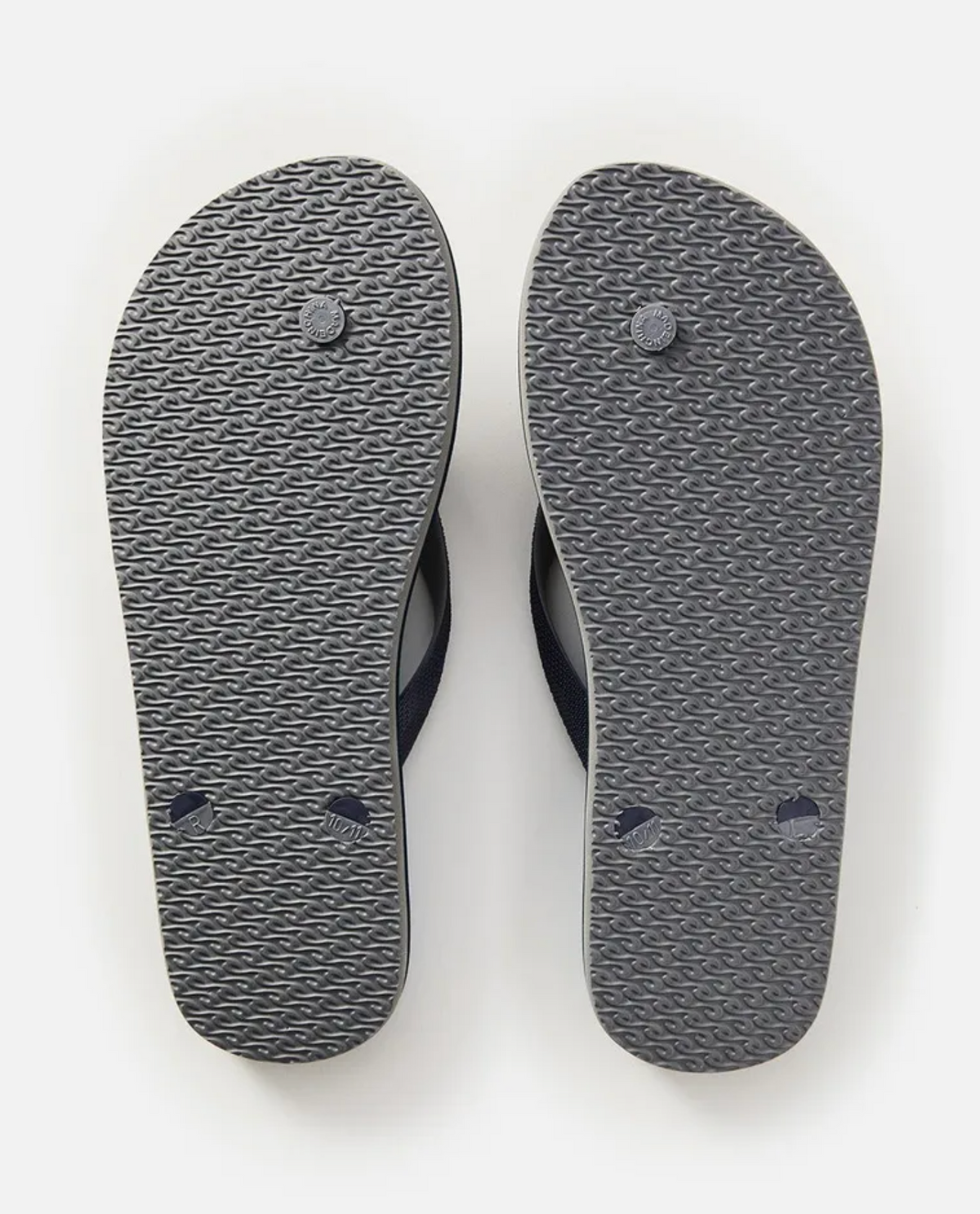 A pair of Rip Curl Iconic Thongs, designed with their signature style, appear from the bottom. The blue flip-flops' textured soles feature circular patterns with some wear and durable rubber straps, resting side by side on a plain white background.