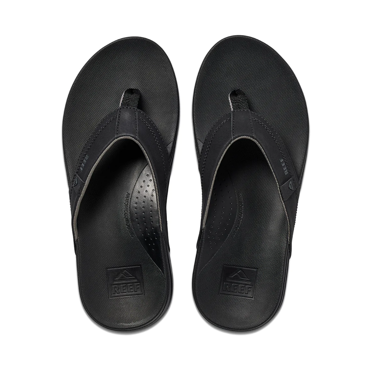 From above, observe a pair of black REEF Cushion Spring flip-flops made from synthetic leather. They have a textured footbed, wide strap with subtle branding, and provide comfortable arch support, ideal for all-day wear.