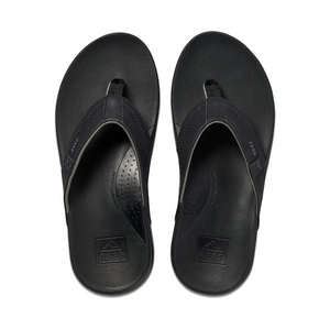From above, observe a pair of black REEF Cushion Spring flip-flops made from synthetic leather. They have a textured footbed, wide strap with subtle branding, and provide comfortable arch support, ideal for all-day wear.