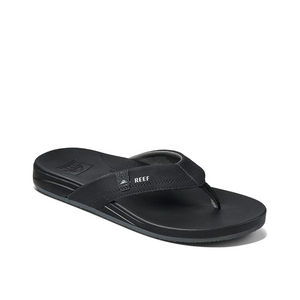 The REEF Cushion Spring is a black flip-flop with a textured sole and straps, providing comfort with arch support. It features the "REEF" brand on the strap and offers a sleek synthetic leather design, ideal for casual wear.