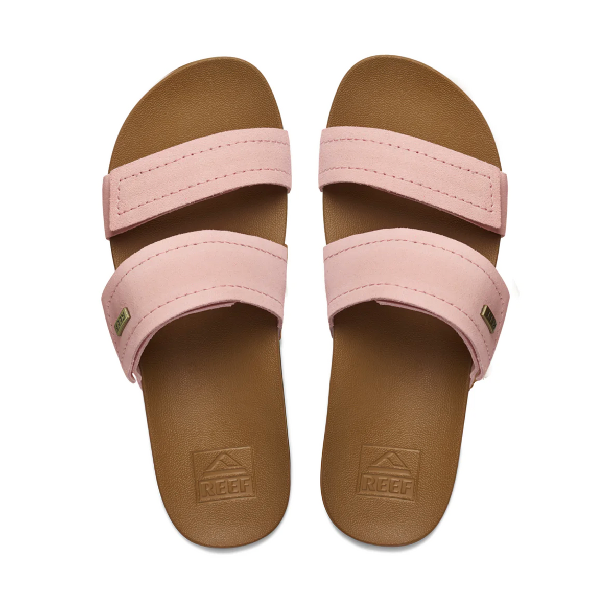 The REEF Velcro Vista SE pink slide sandals feature premium leather double straps, a brown footbed with "REEF" embossed near the heel, and a cushion bounce midsole. They are displayed on a white background.