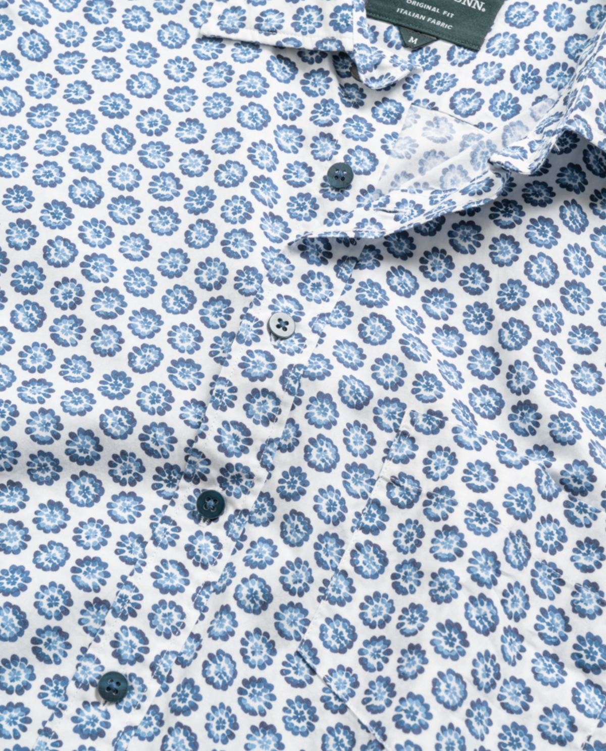 Close-up of the Rodd & Gunn First Avenue Shirt, showcasing a blue and white floral pattern. This 100% cotton button-up features intricate blue flowers on a white background, visible buttons down the center, and a stylish spread collar.