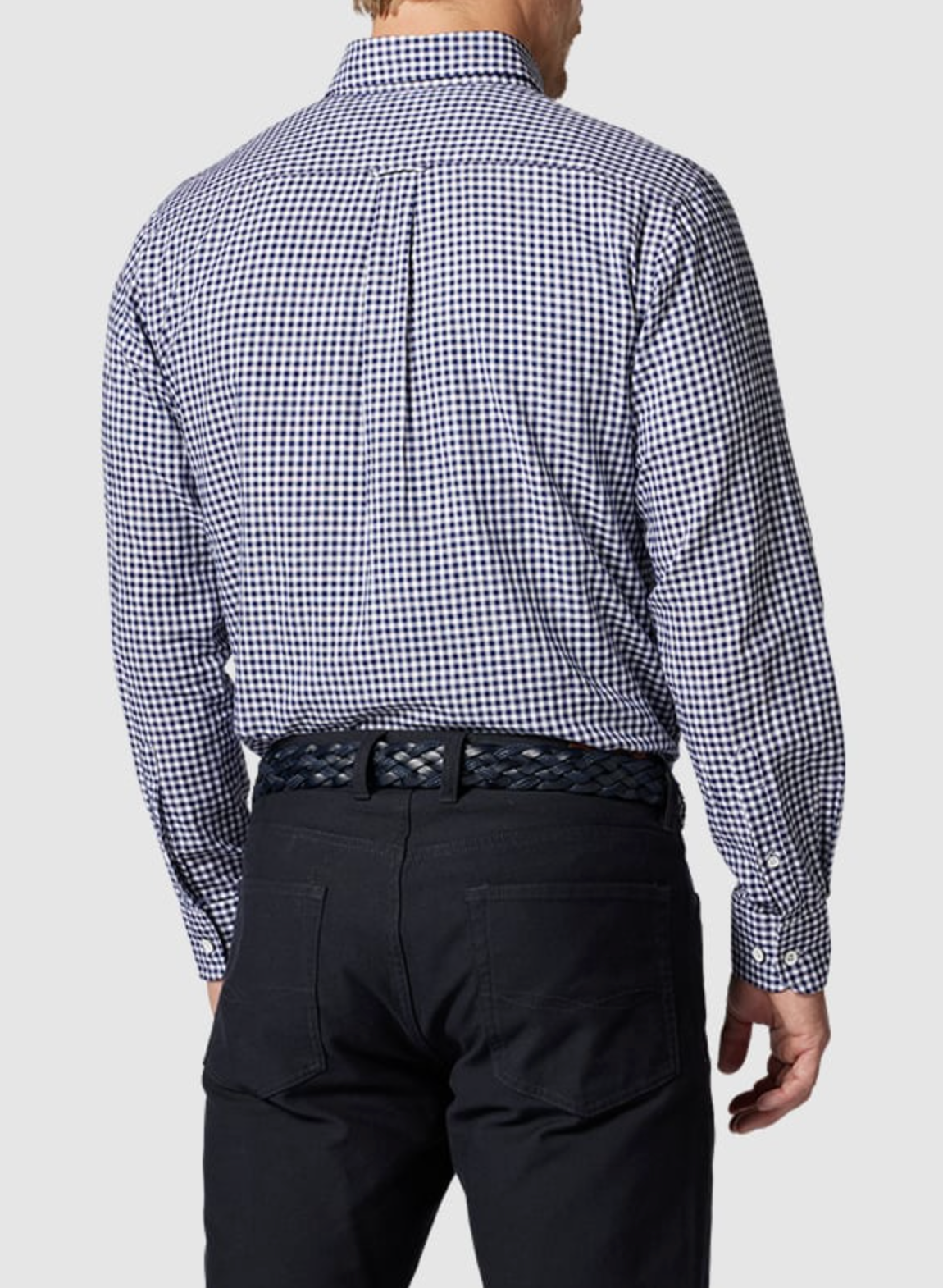 The person is wearing a Rodd & Gunn Superfine Gunn Check Oxford Sports Fit Shirt in blue and white check, made of 100% cotton, along with black pants and a braided black belt, facing away from the camera.